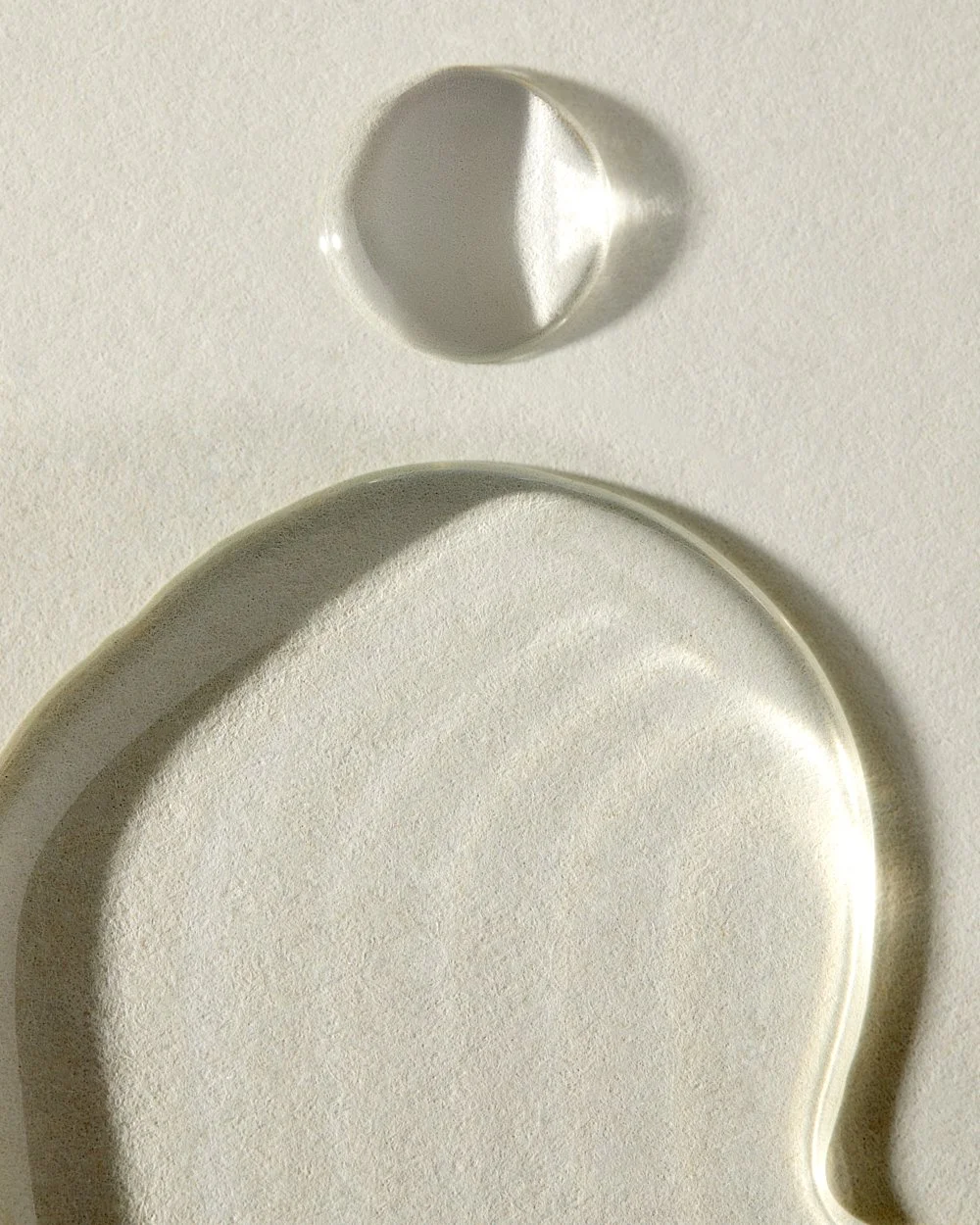 Close-up of a water droplet resting on rippled sand-toned texture, by Adrianna Favero.
