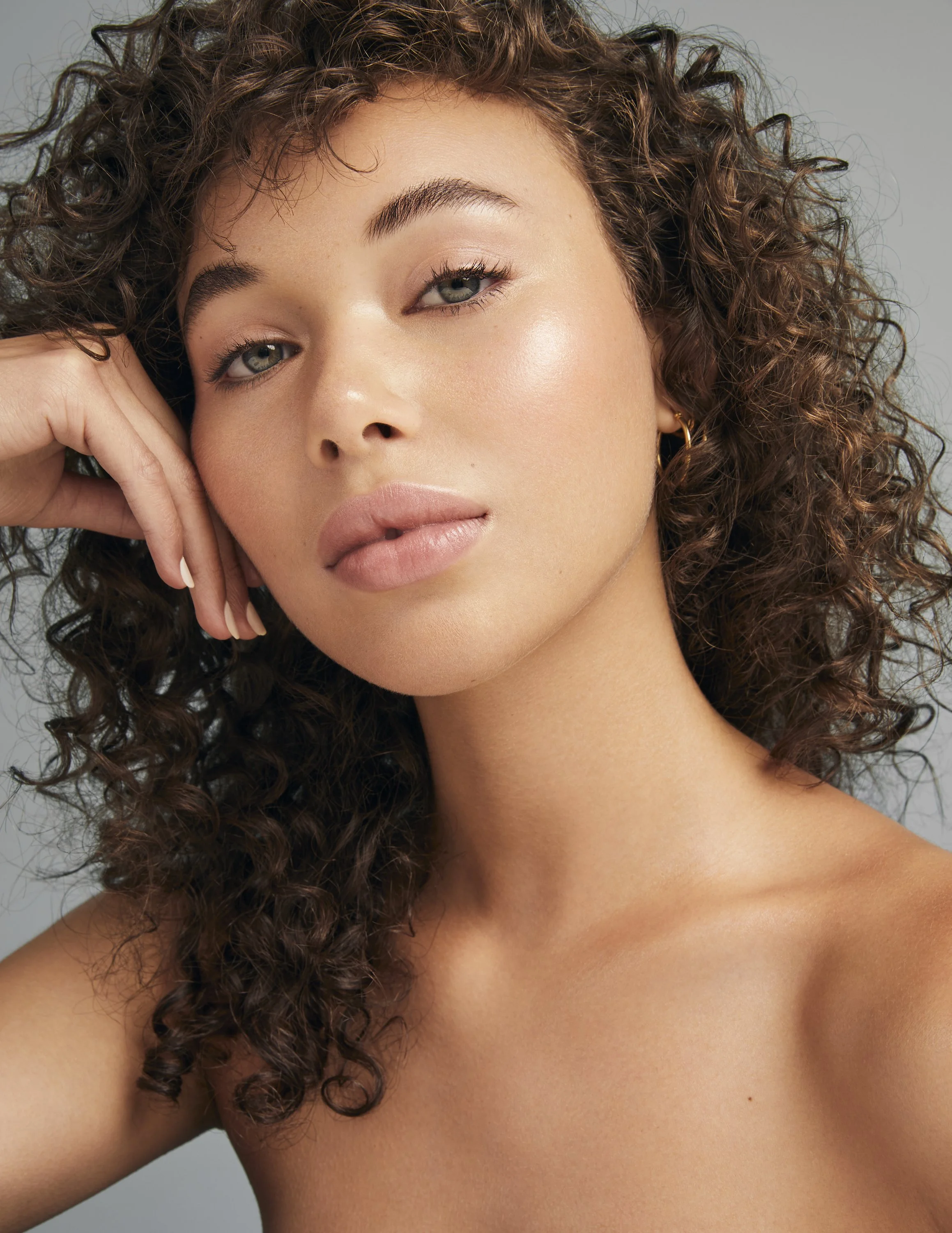 Portrait of a person with curly brown hair, resting their head on their hand in a relaxed pose, with a neutral background.