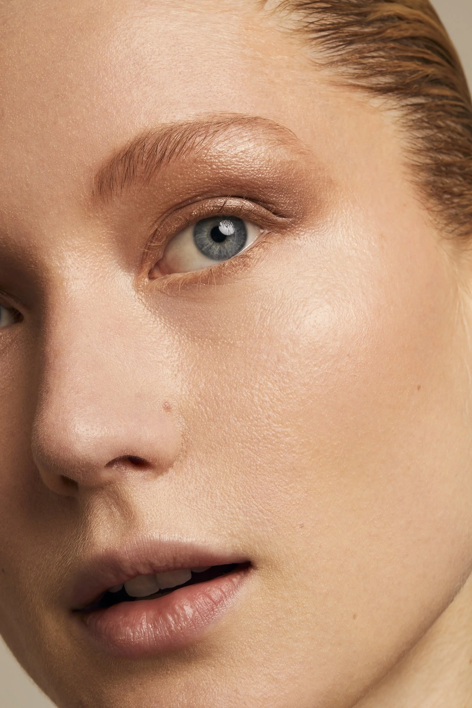 Close-up of a woman's face focusing on one eye, eyebrow, smooth skin, and lips, with natural makeup highlighting the eye area.