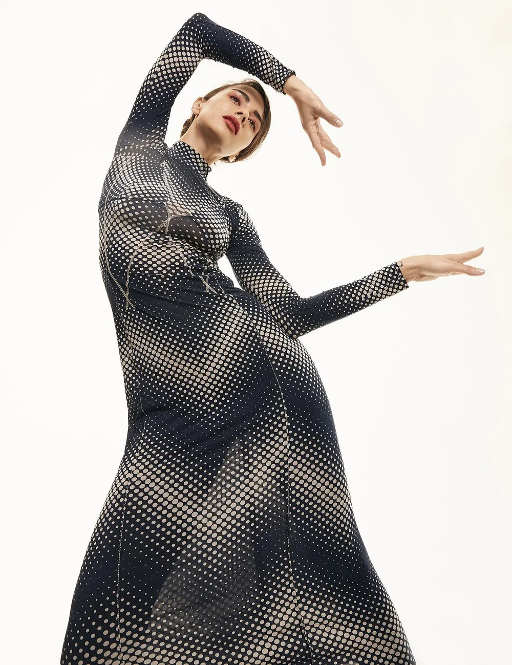 Person wearing long-sleeved polka-dot dress posing dramatically against a light background.