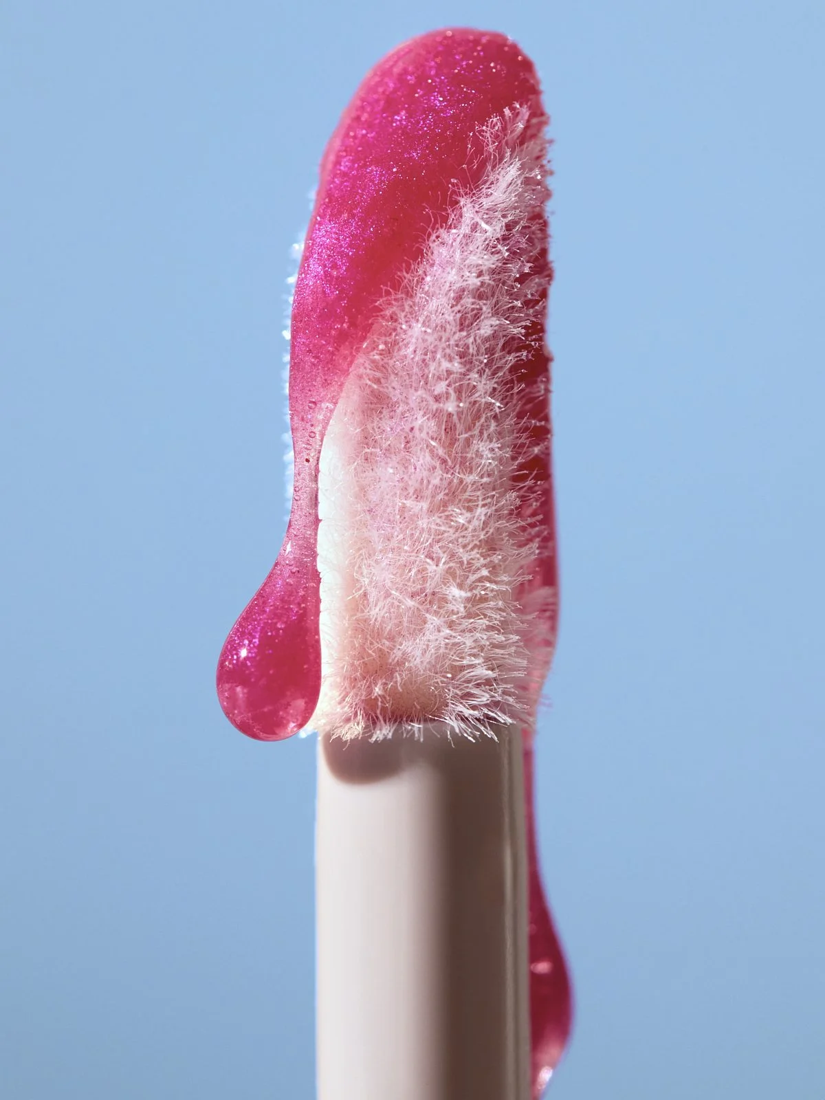 Close-up of a sparkly pink lip balm bullet against a sky blue background, by Adrianna Favero.