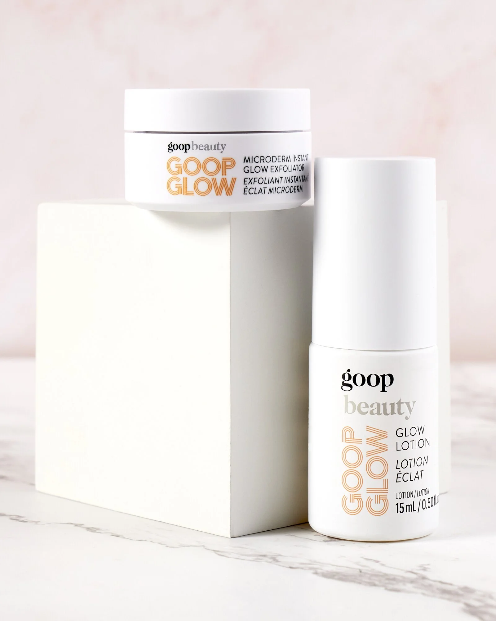 Goop Glow beauty products, including a jar of Microderm Instant Glow Exfoliator and a bottle of Glow Lotion, displayed on a marble and white surface.