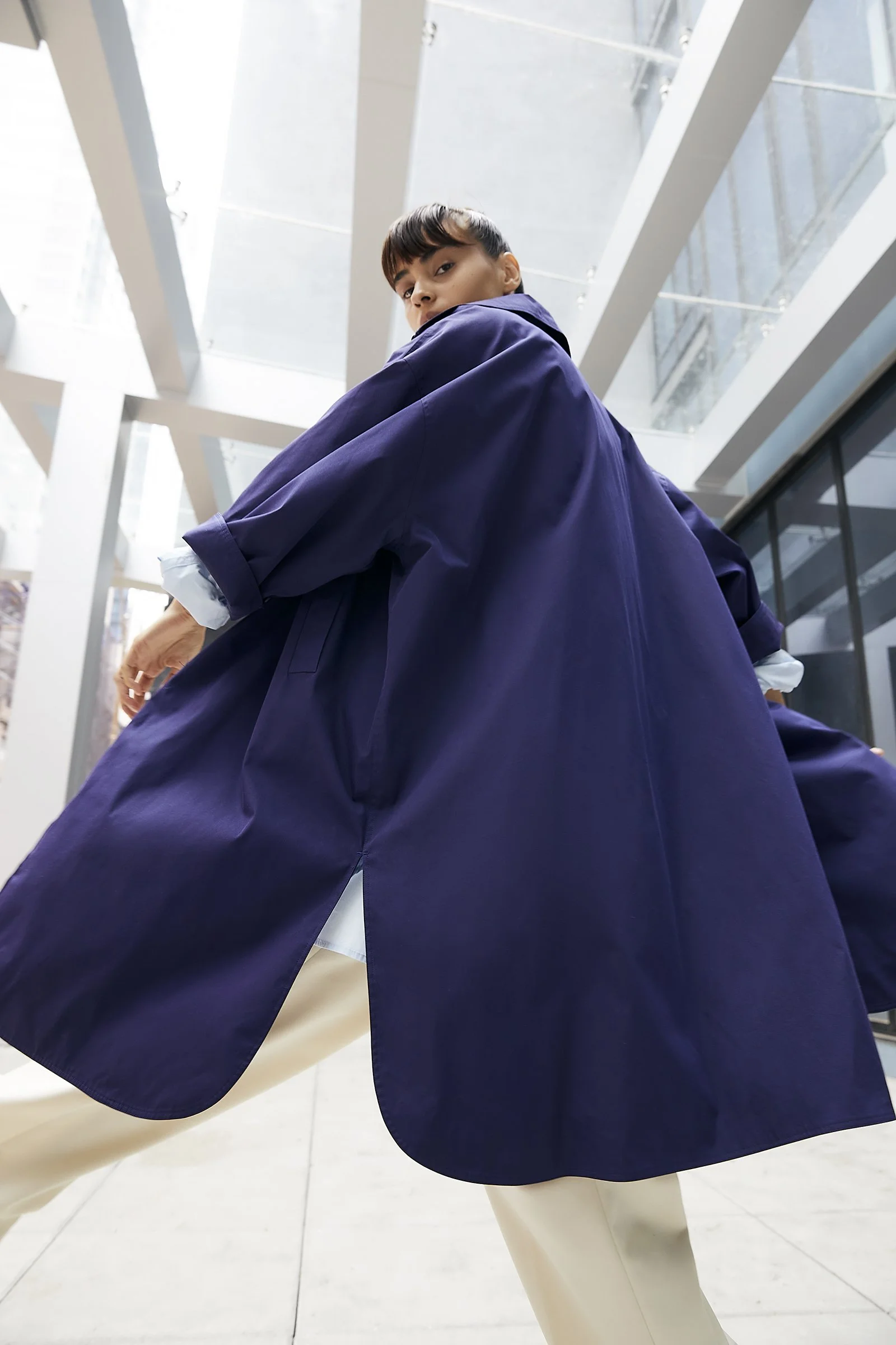 Person wearing a blue coat, standing in a modern building with glass and concrete architecture.