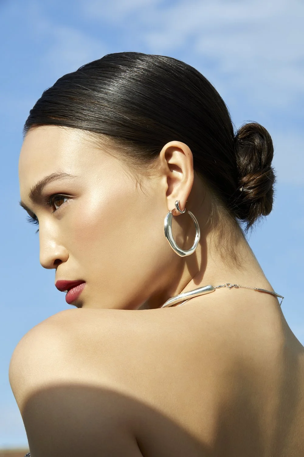 Profile of a woman with a bun hairstyle and hoop earrings against a blue sky.