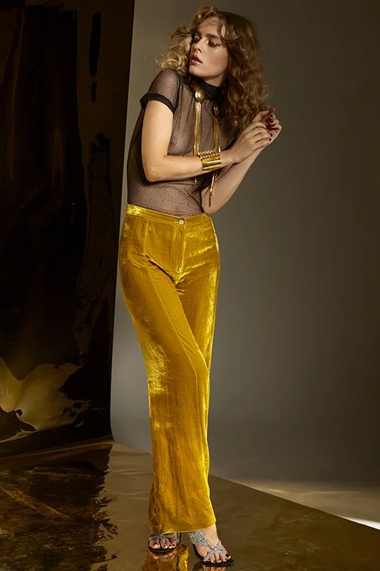 FAJO Magazine holiday fashion editorial: full-length shot of a model in mustard wide-leg trousers and a black top leaning against a wall, photographed by Adrianna Favero.