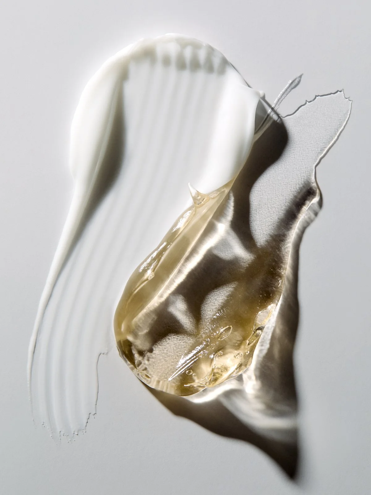 Close-up texture shot of white cream swirled with a gold liquid streak, by Adrianna Favero.