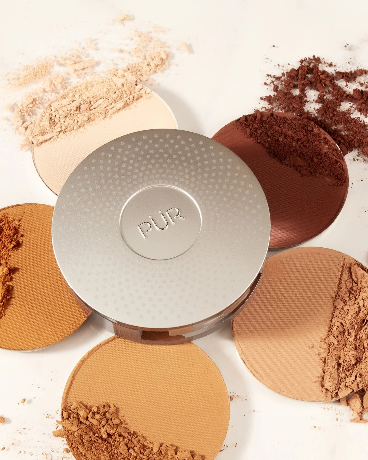 Assorted face powders in various shades with a PUR branded compact, on a light background.