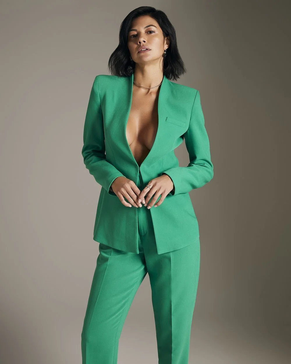Woman wearing a green suit with no shirt, short black hair, neutral background