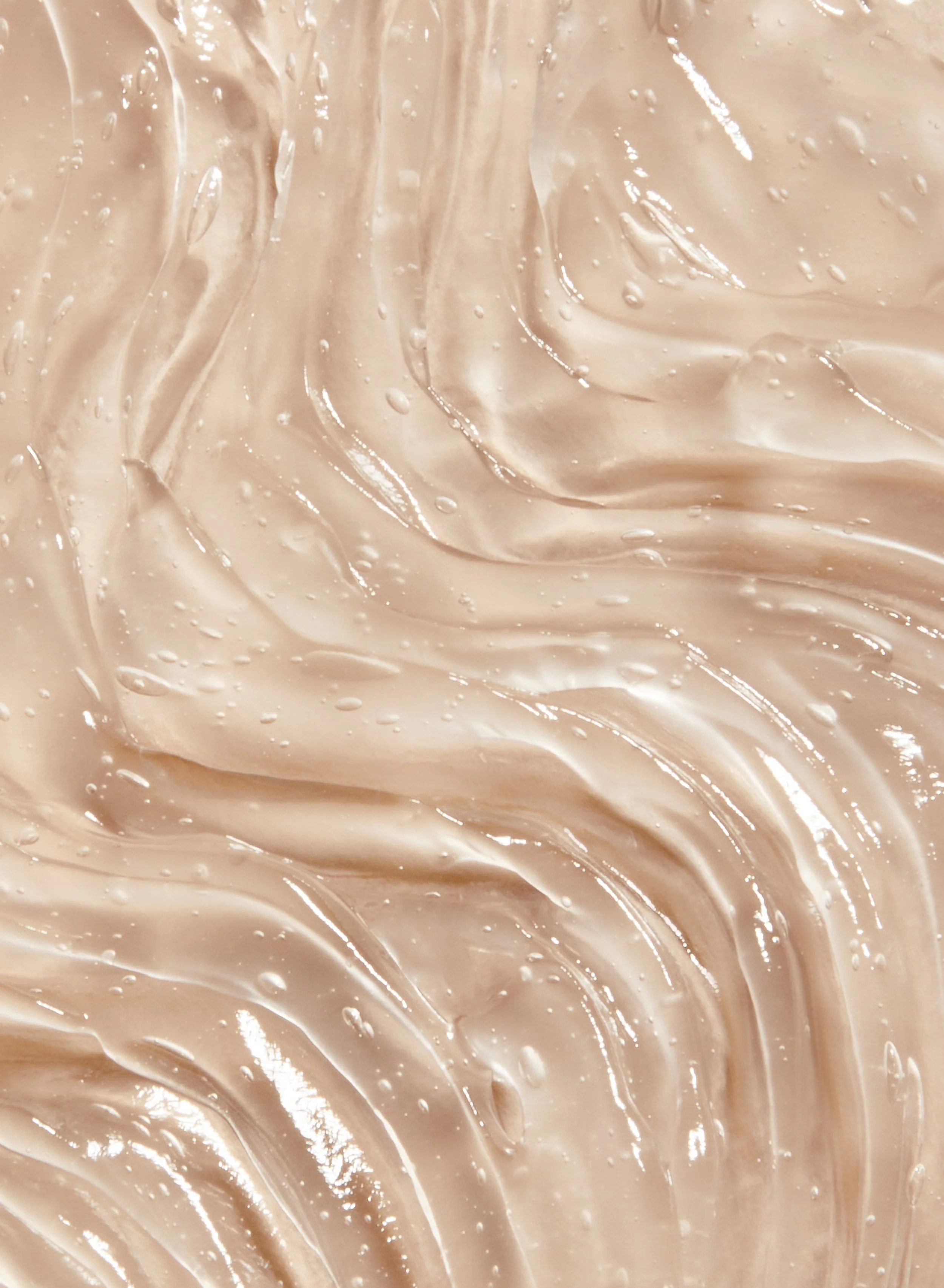 Close-up of beige creamy texture with smooth waves and small droplets.
