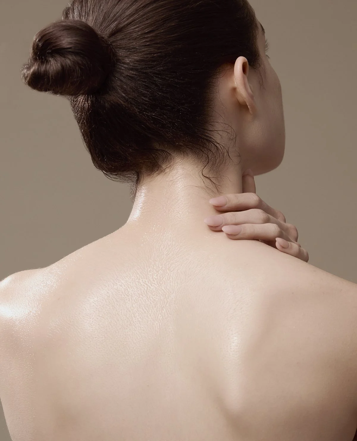 Beauty photography of a model from behind with hair in a bun, hand resting on the nape of her neck, highlighting smooth skin for a skincare and beauty brand campaign by Adrianna Favero, NYC beauty photographer and director.