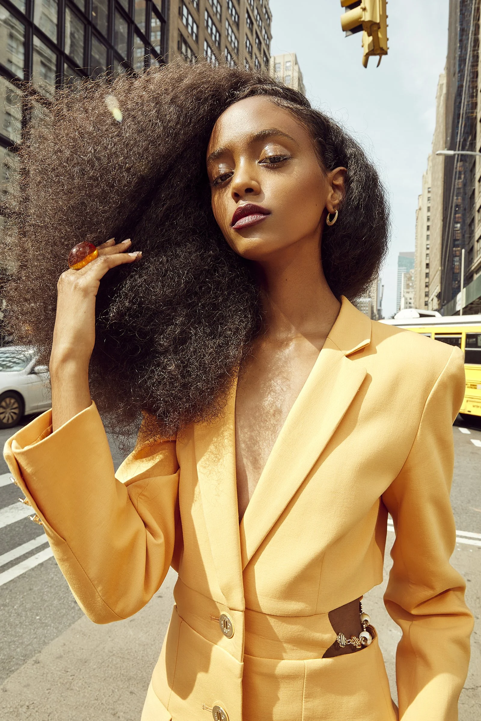 Fashion model in yellow suit on city street with skyscrapers and yellow school bus in background.