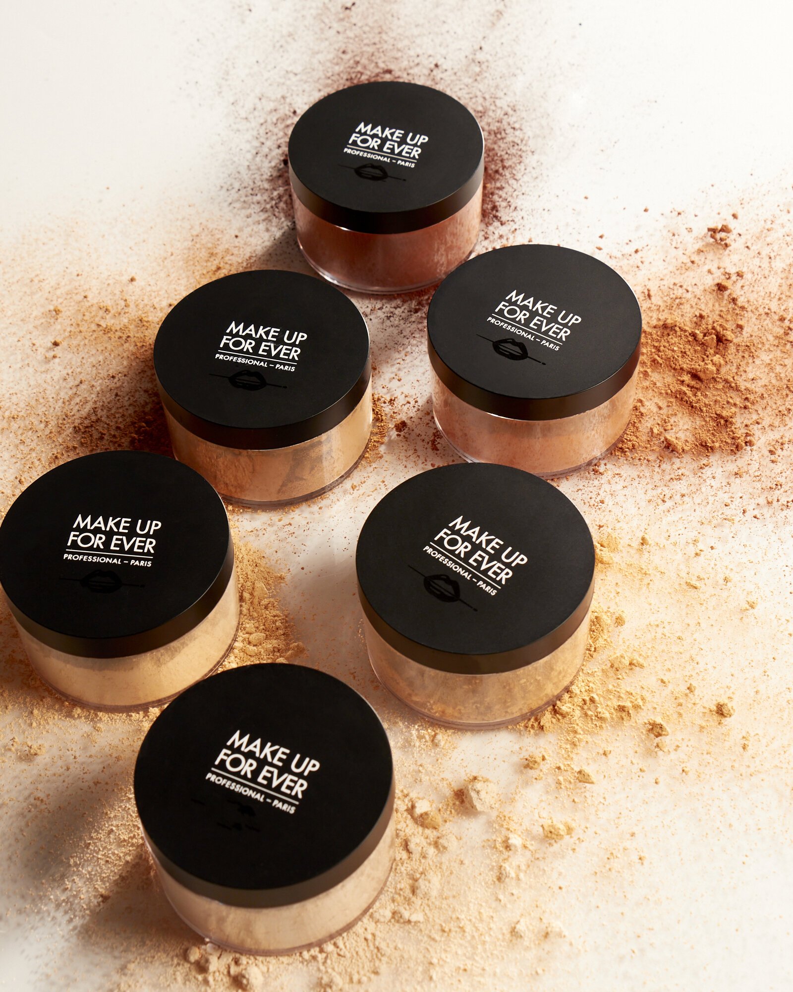 Loose setting powder containers labeled "Make Up For Ever" with scattered powder on surface.