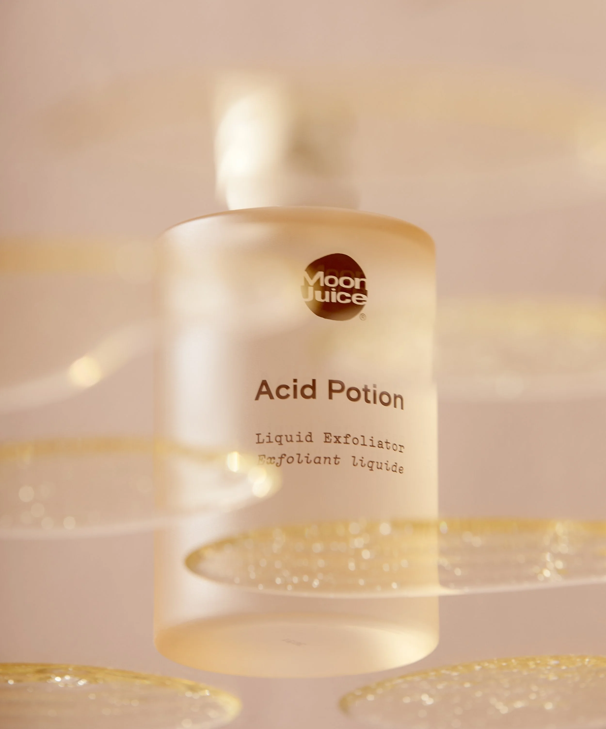 Bottle of Moon Juice Acid Potion liquid exfoliator with floating liquid droplets, featuring a soft focus and beige background.