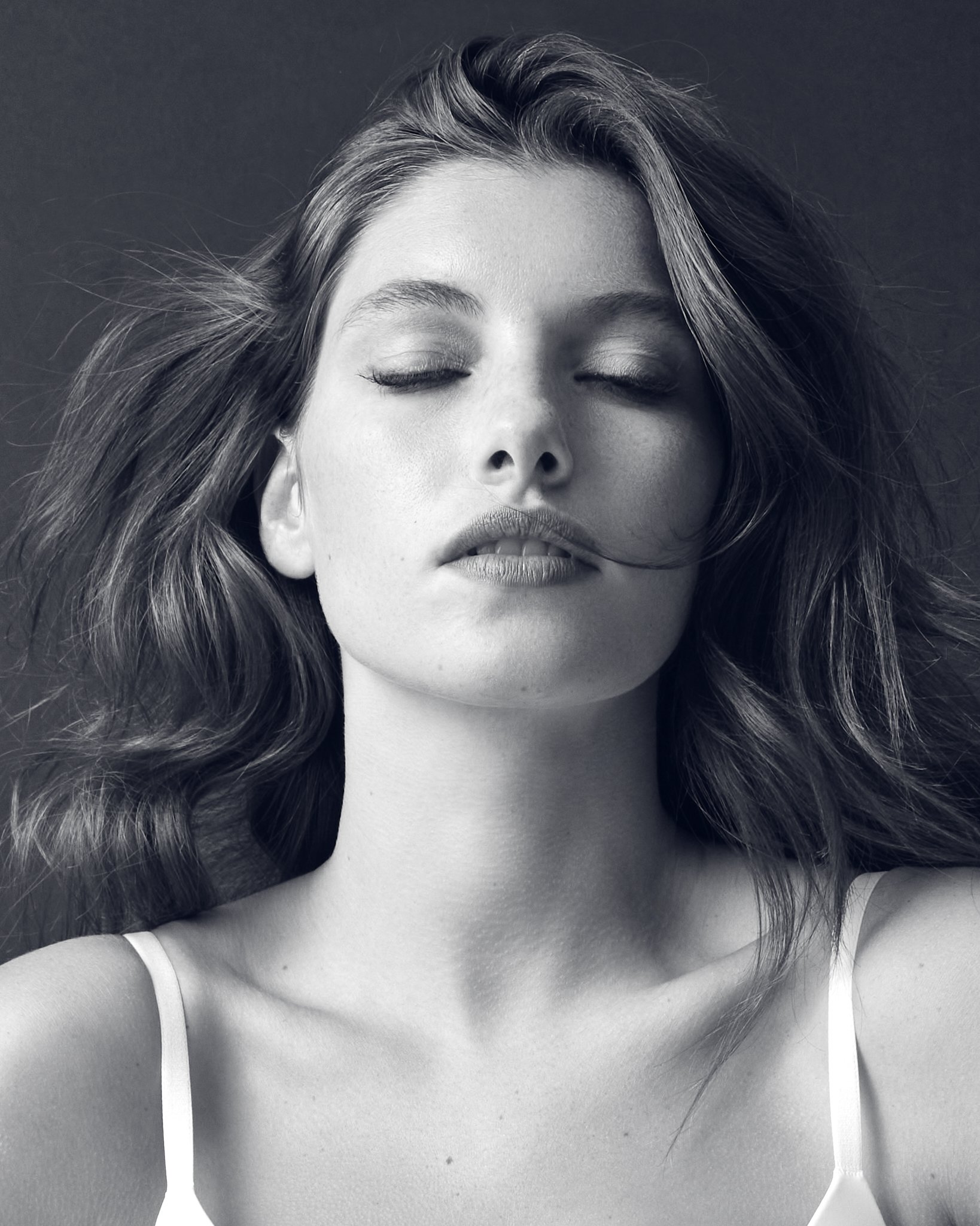 Black and white portrait of a woman with closed eyes and slightly tousled hair, wearing a spaghetti strap top.