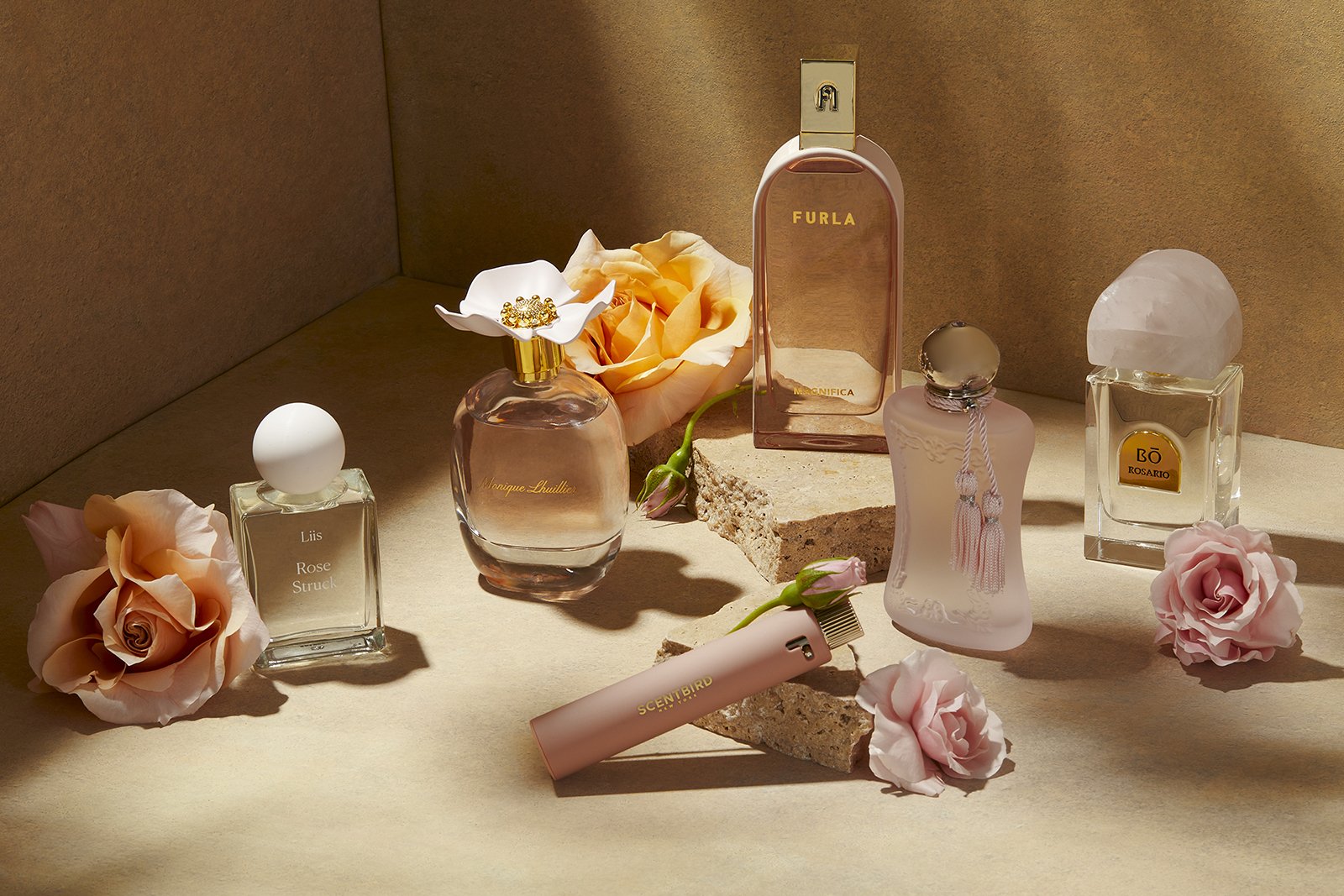 Various perfume bottles displayed with pink and orange roses on a textured surface, under soft lighting.
