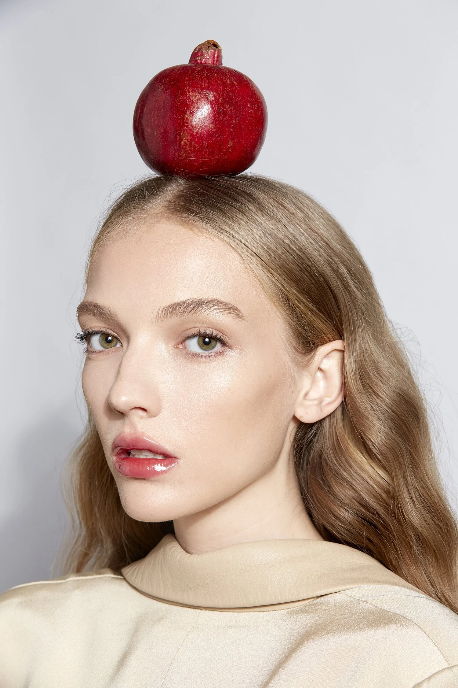 Woman with a pomegranate on her head, wearing a light beige top.