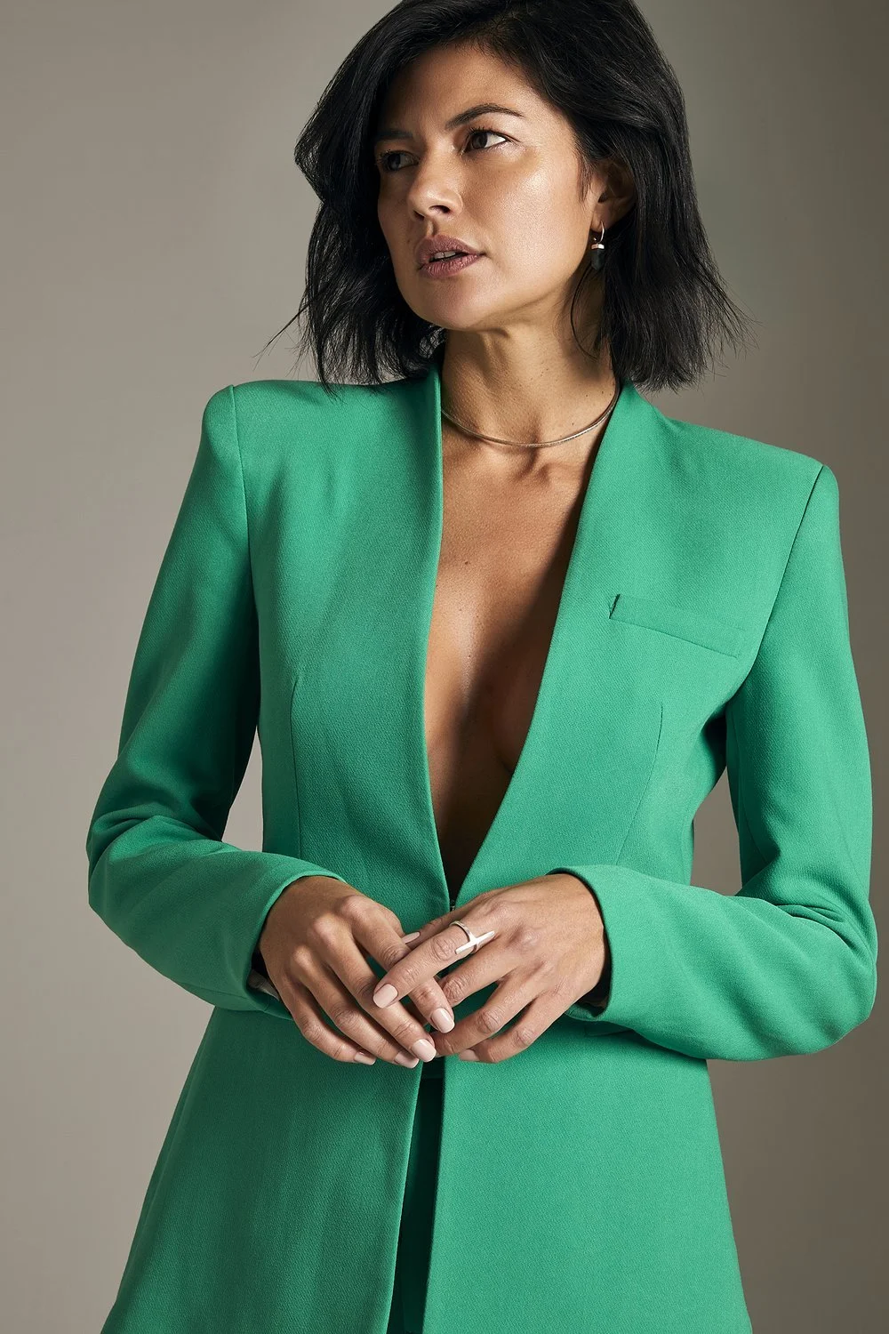 Woman in green blazer with short black hair, wearing a ring and necklace.