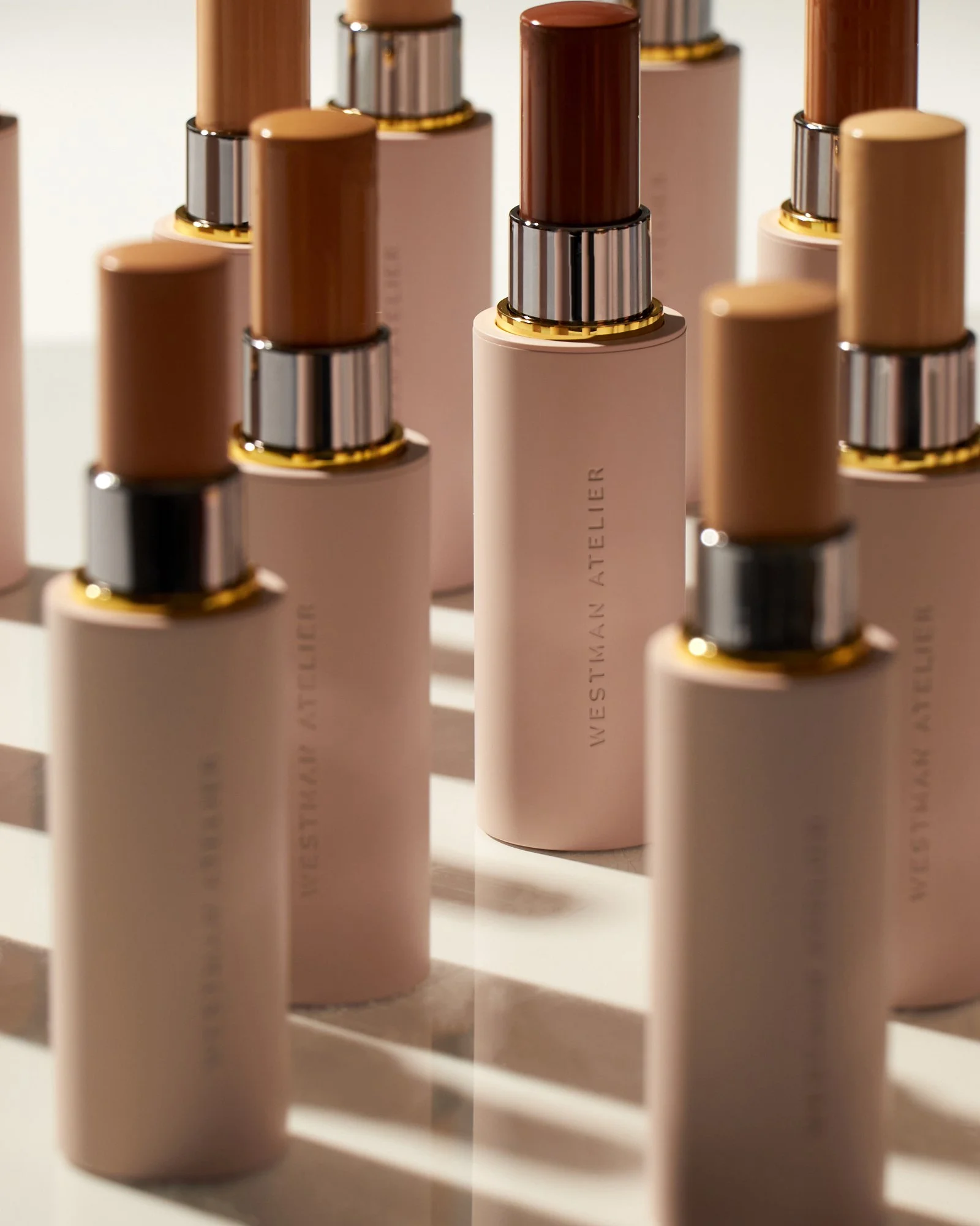 Assorted cosmetic foundation sticks in various shades with "Westman Atelier" branding, arranged in a staggered formation.