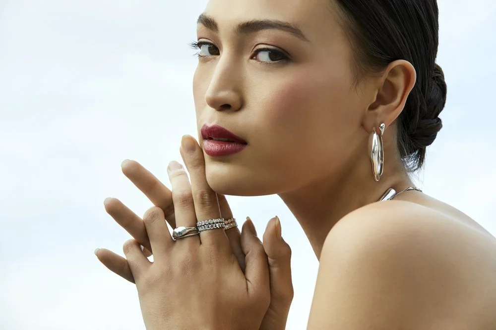 Woman wearing silver jewelry, including earrings and rings, looking to the side.