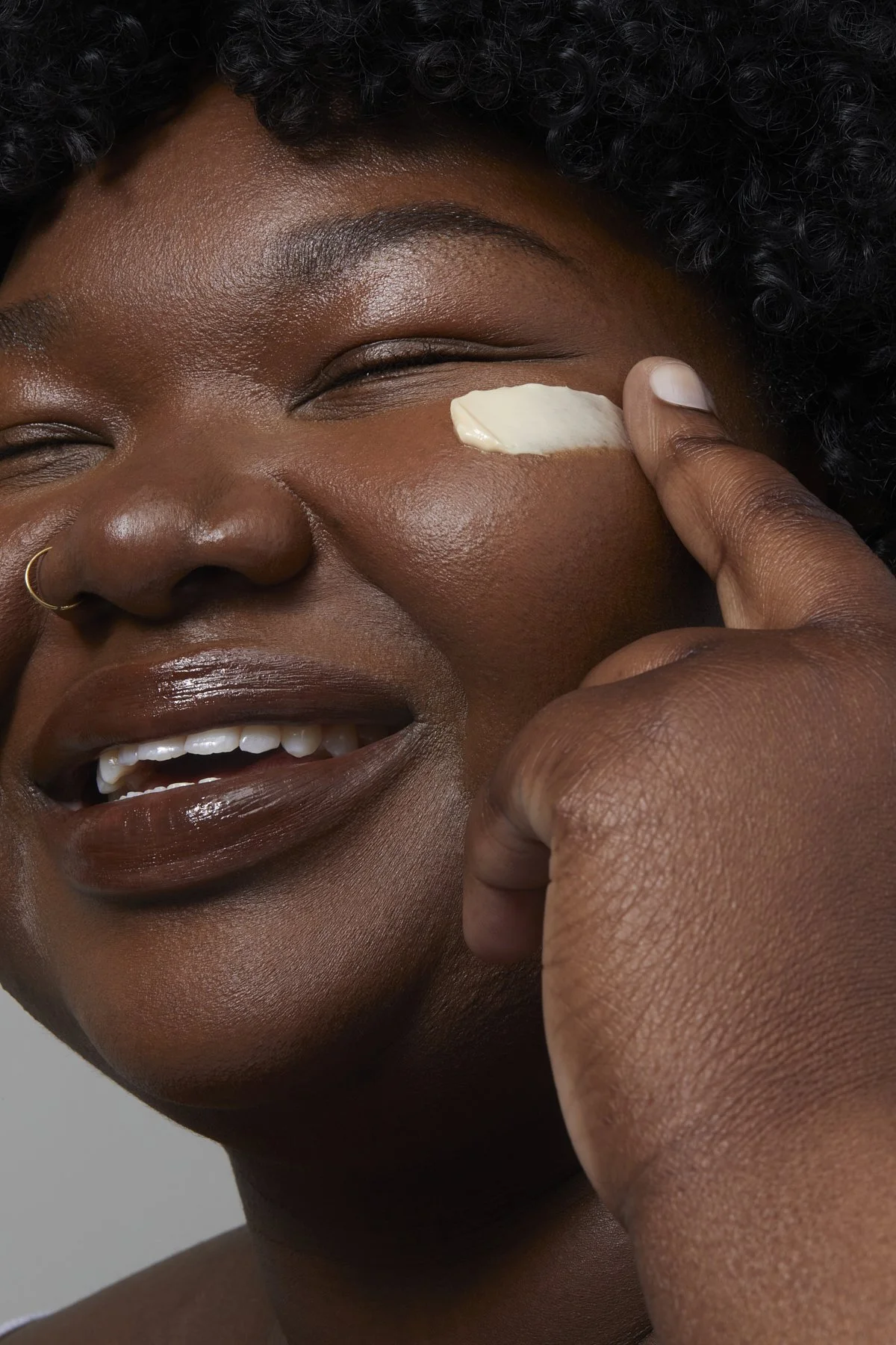 Brownkind skincare campaign: smiling model applying cream beneath her eye with her fingertip, photographed by Adrianna Favero.
