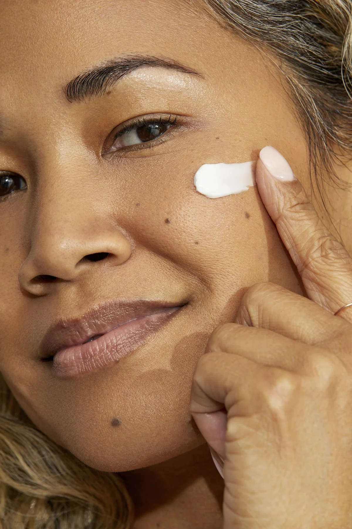 Brownkind skincare campaign: close-up of model applying cream to her cheek with her fingertips, photographed by Adrianna Favero.