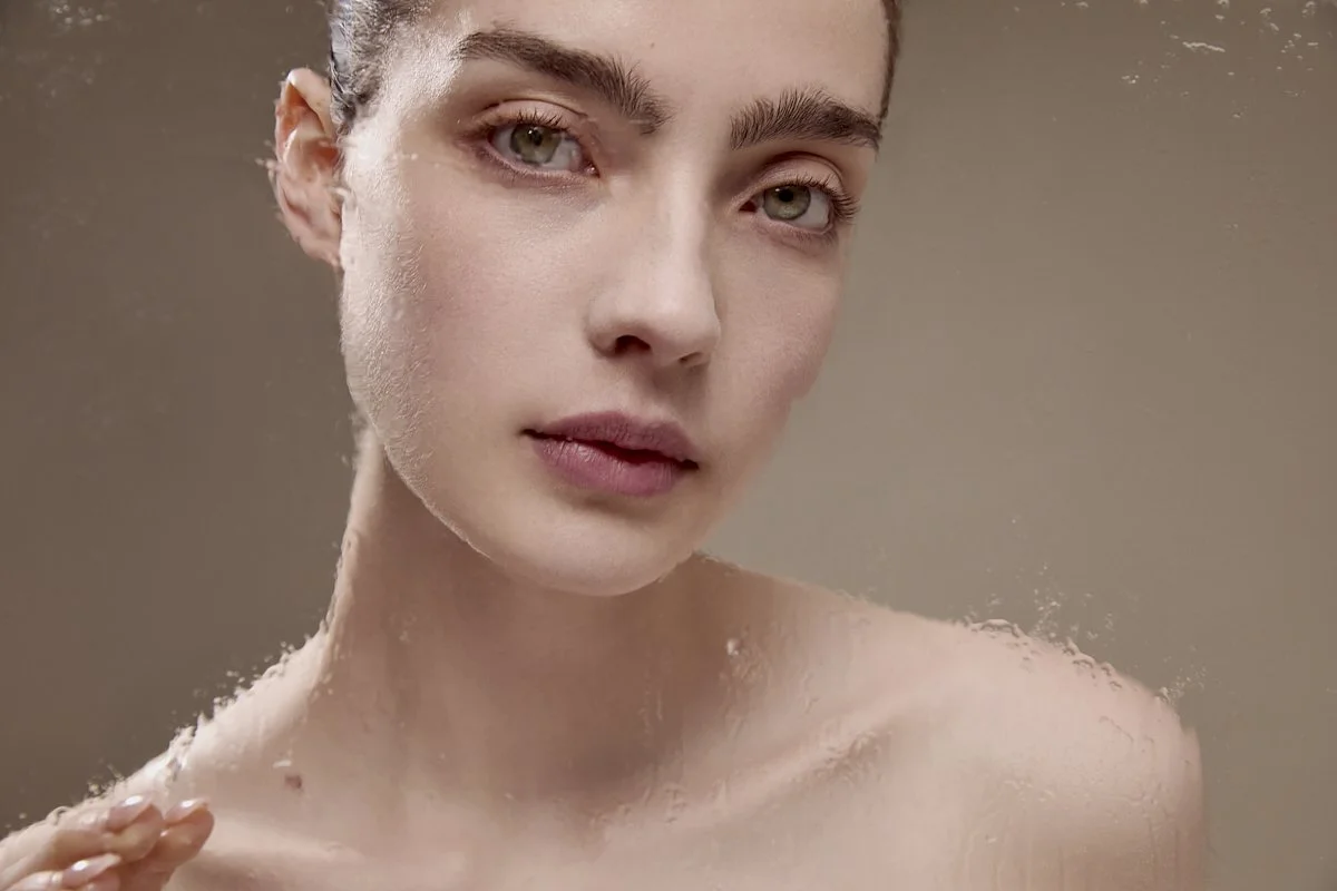 Soft, warm-toned beauty portrait of a model with bare shoulders and natural makeup, by Adrianna Favero.