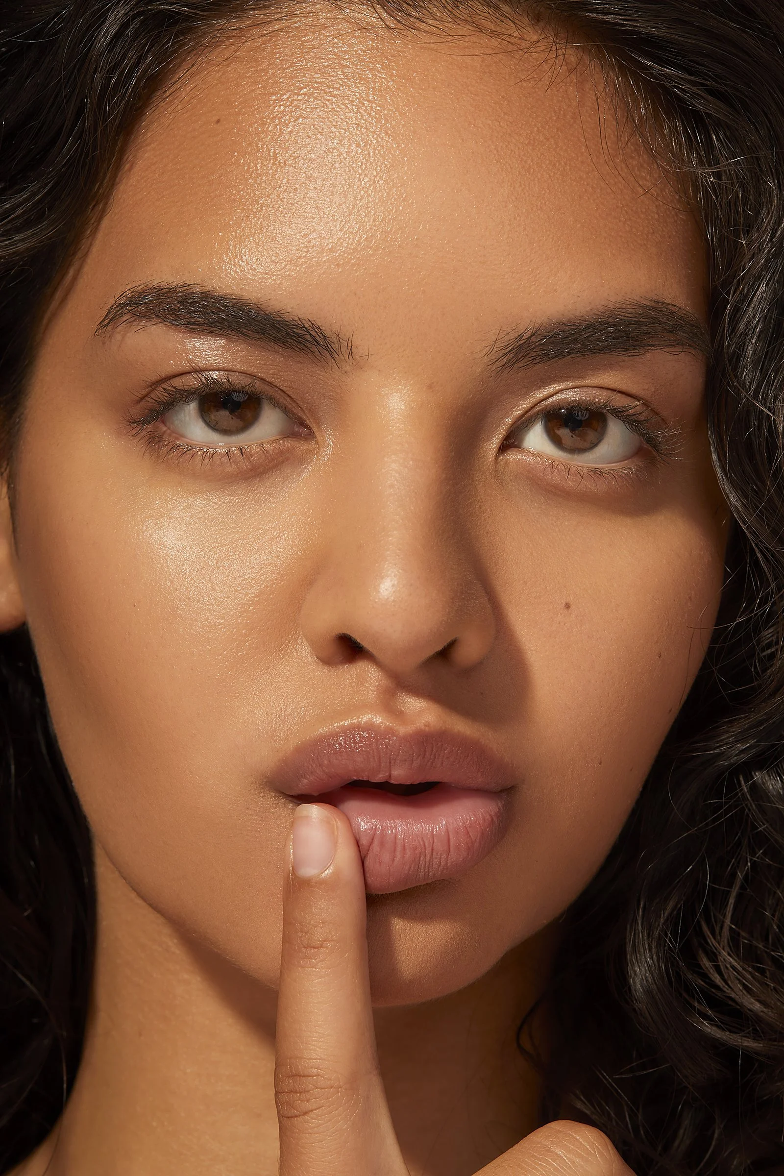 Close-up of a person's face with finger on lips, demonstrating smooth skin and natural makeup.