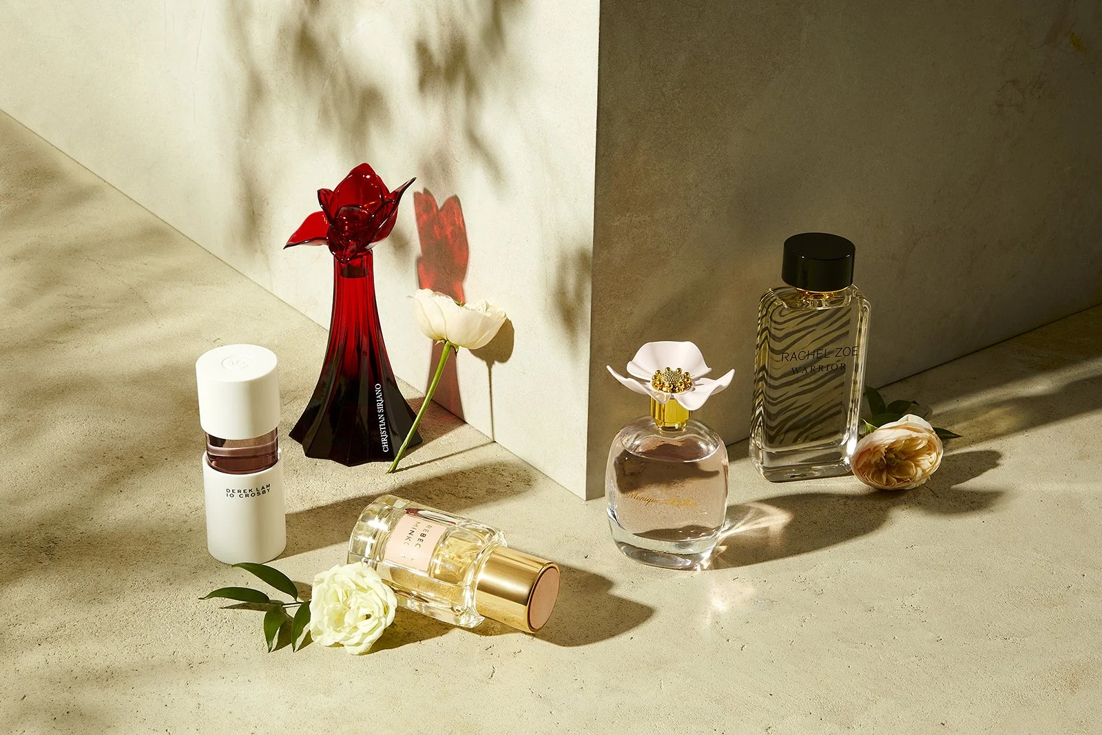 Collection of perfume bottles displayed on a concrete surface with decorative flowers, featuring various shapes and designs, including a red sculpted bottle and a zebra-patterned bottle.