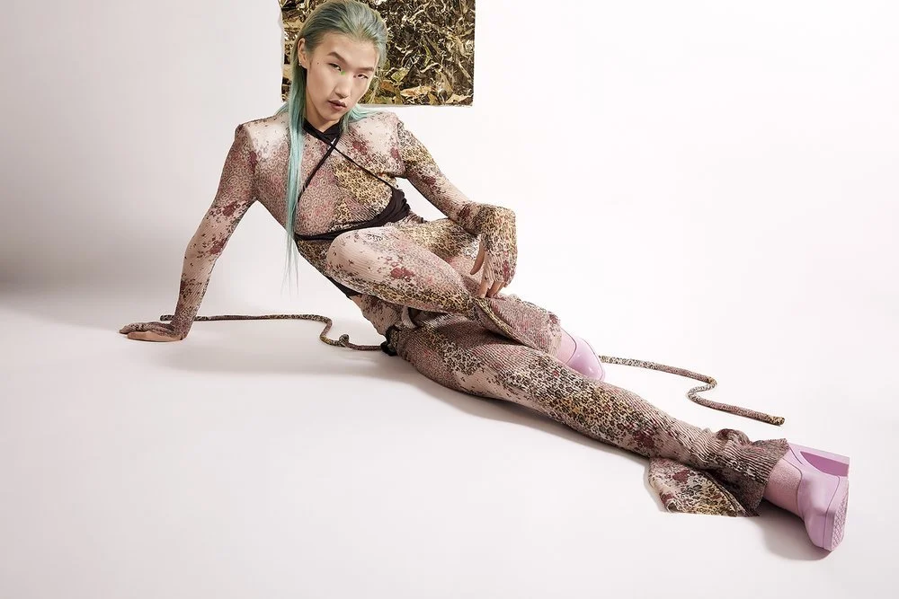 Person posing in patterned bodysuit and lavender shoes on white background