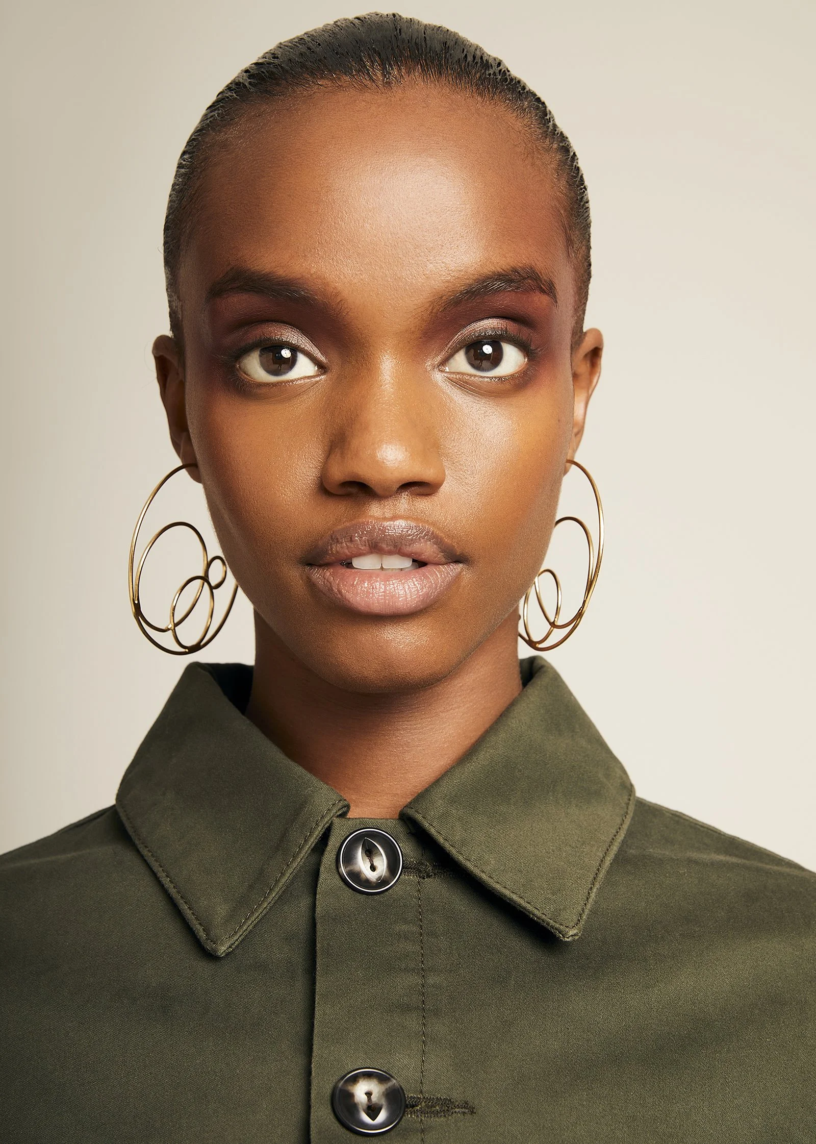 Close-up of a person wearing hoop earrings and a green button-up shirt.