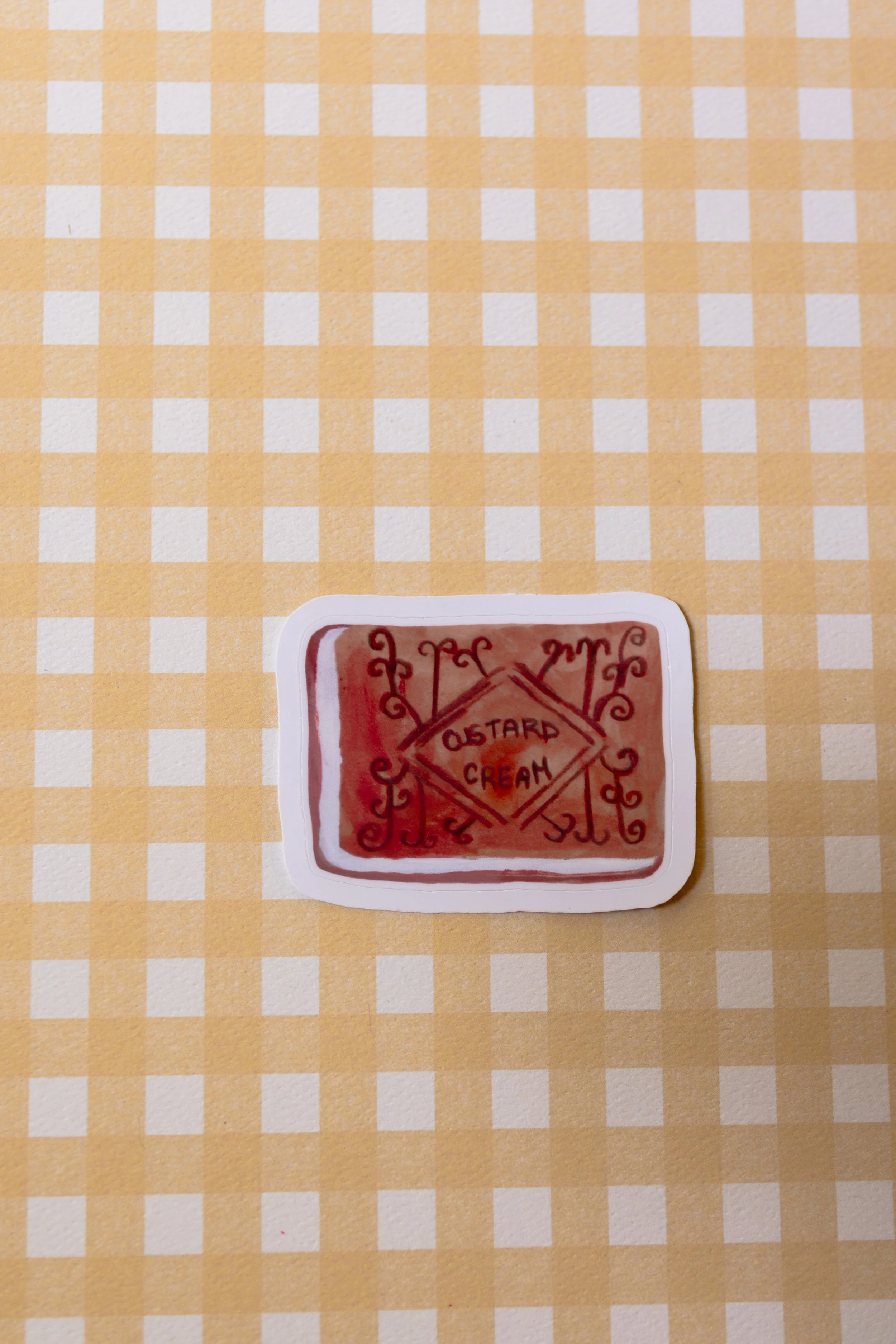 Custard cream cookie sticker on a yellow gingham background.