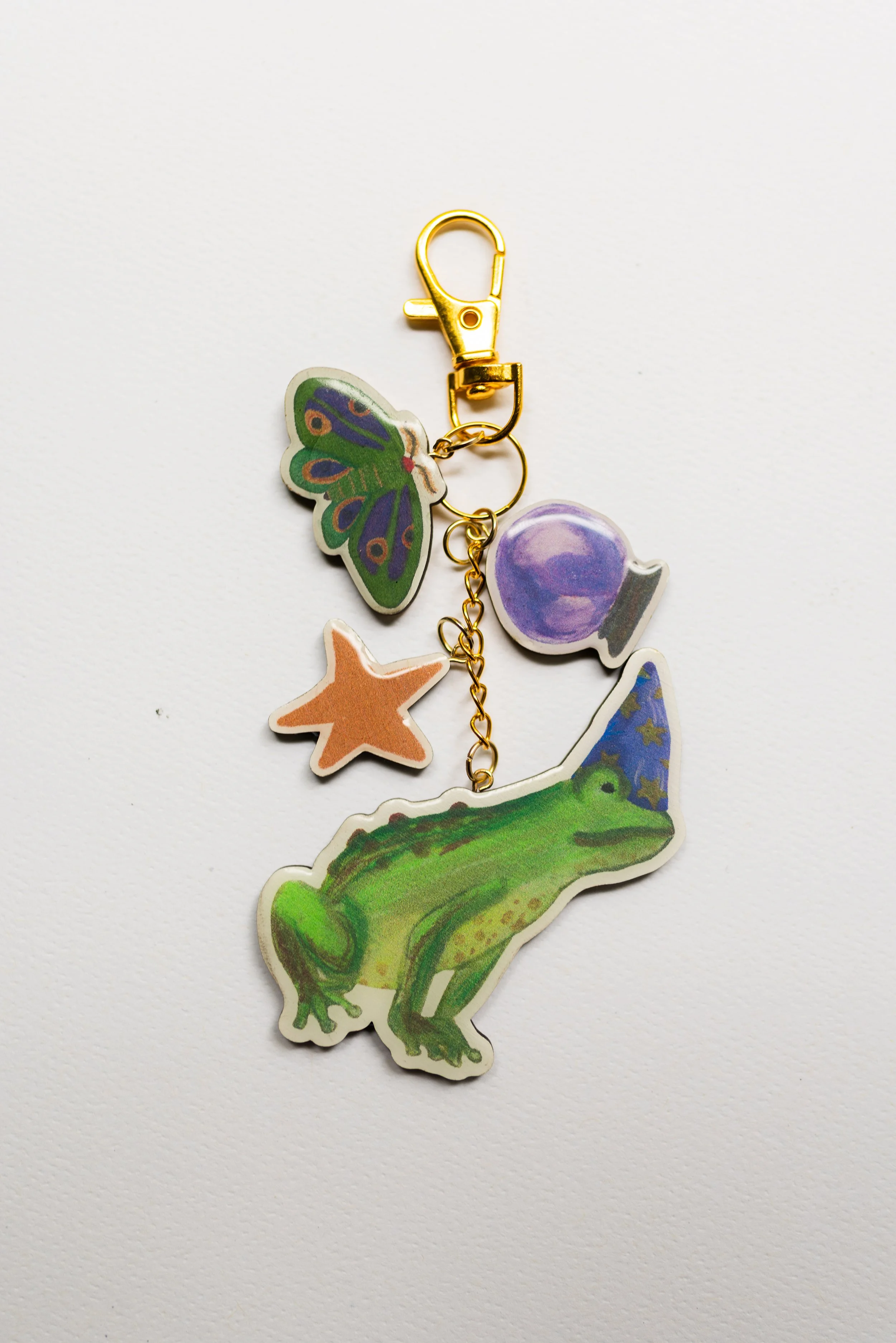Wooden keychain featuring a whimsical green frog in a starry witch hat with moth, crystal ball, and star charms.