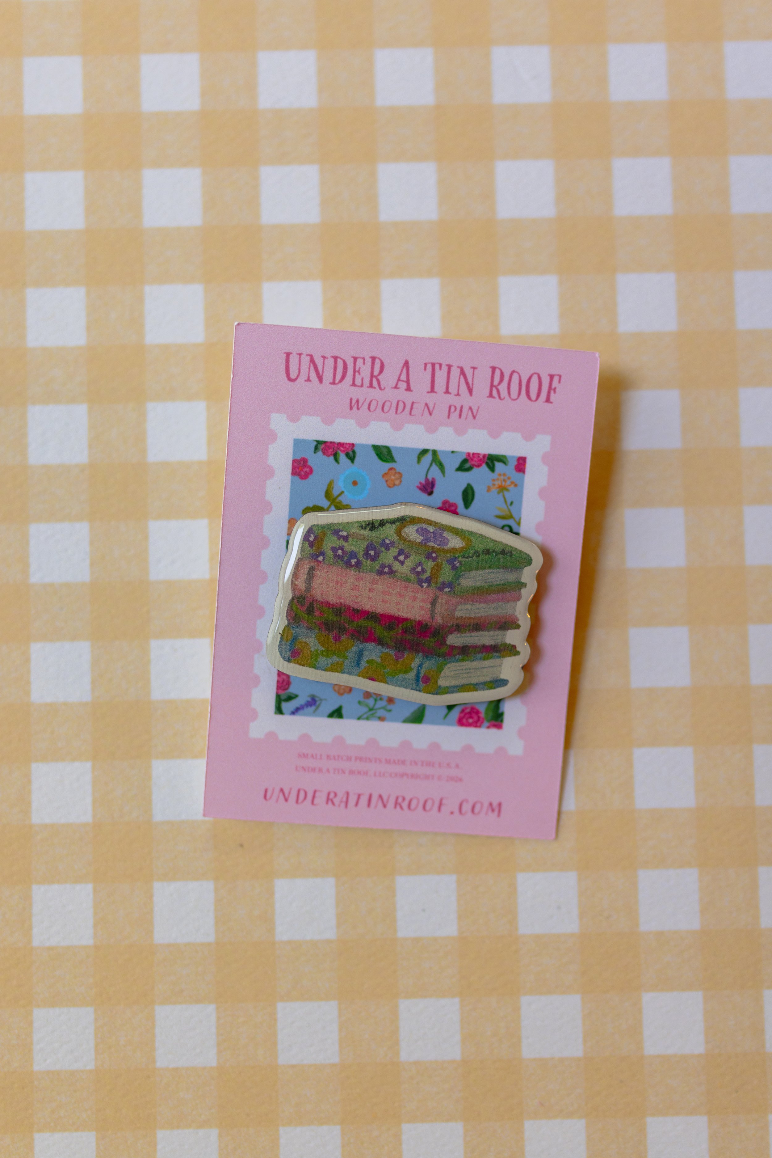 Book lover wooden pin displayed on branded backing card showing full-color printed floral book stack artwork.