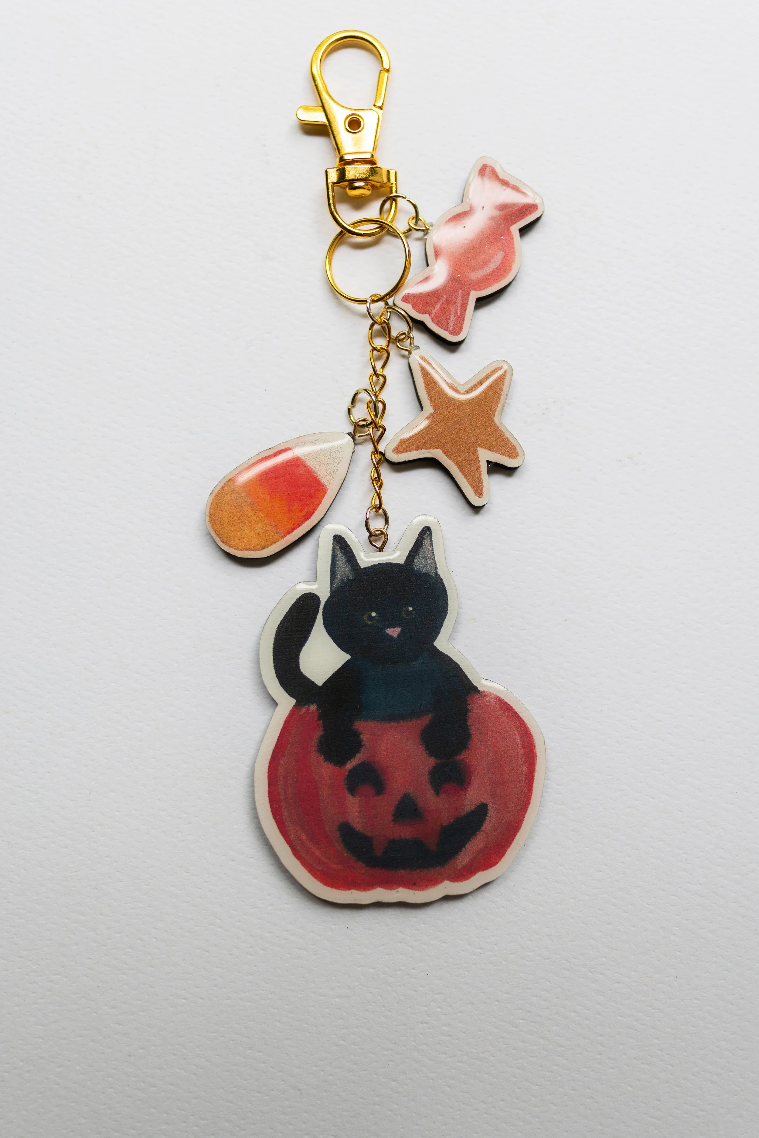 Wooden Halloween keychain featuring a black cat sitting inside a jack-o'-lantern with candy corn, candy, and star charms.