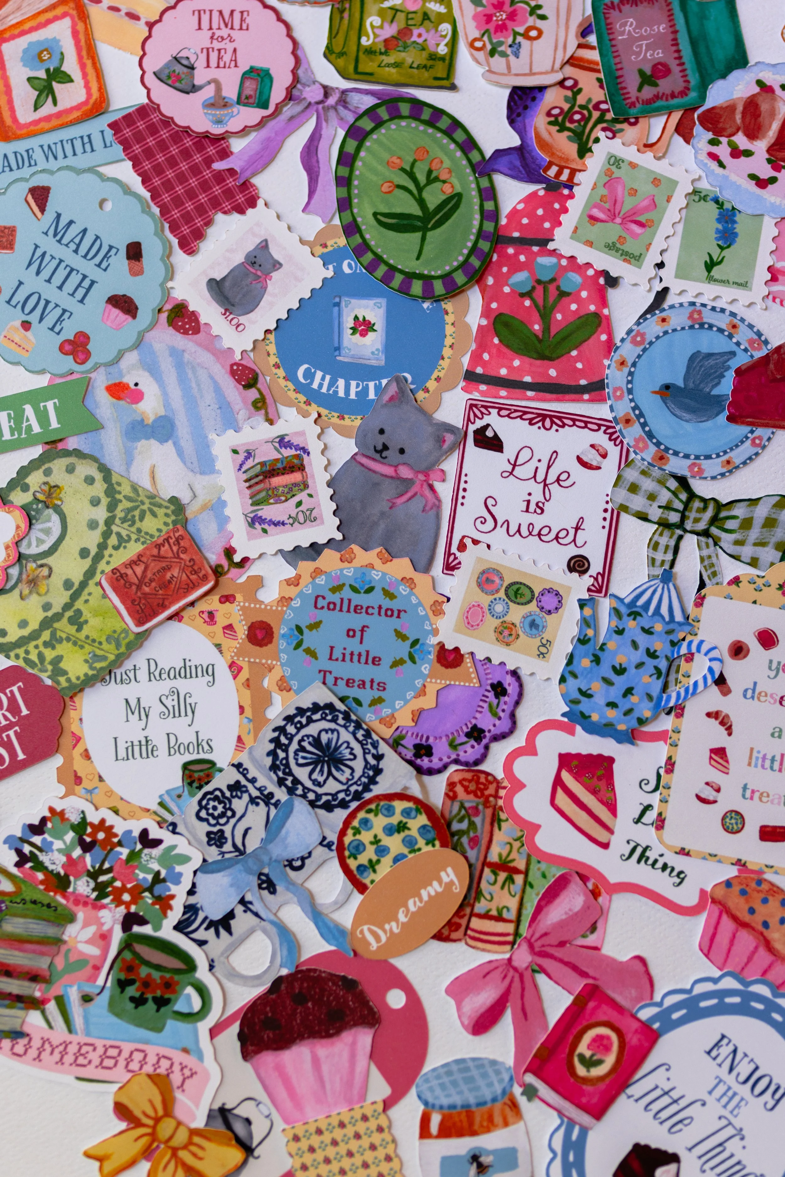 Scrapbook embellishments including books, teacups, desserts, flowers, bows, vintage labels, and journal prompts.