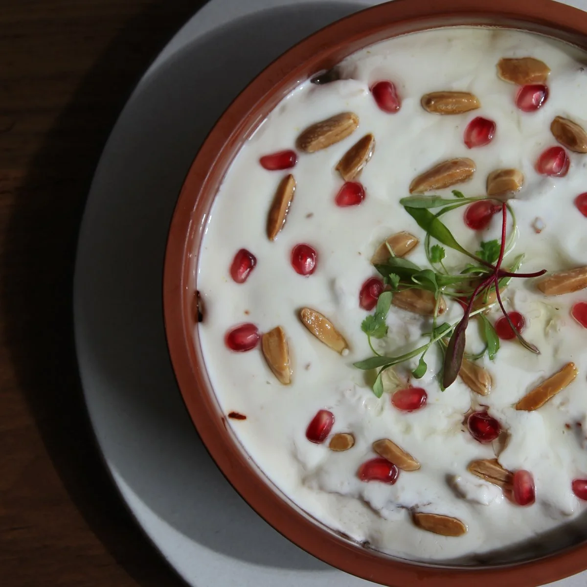 Levantine lunch dish Fattet Jaj served at Ammatoli. Round ramkin of chicken, rice, and garlic, covered in yogurt and olive oil, topped with toasted almonds and fresh pomegranate seeds.