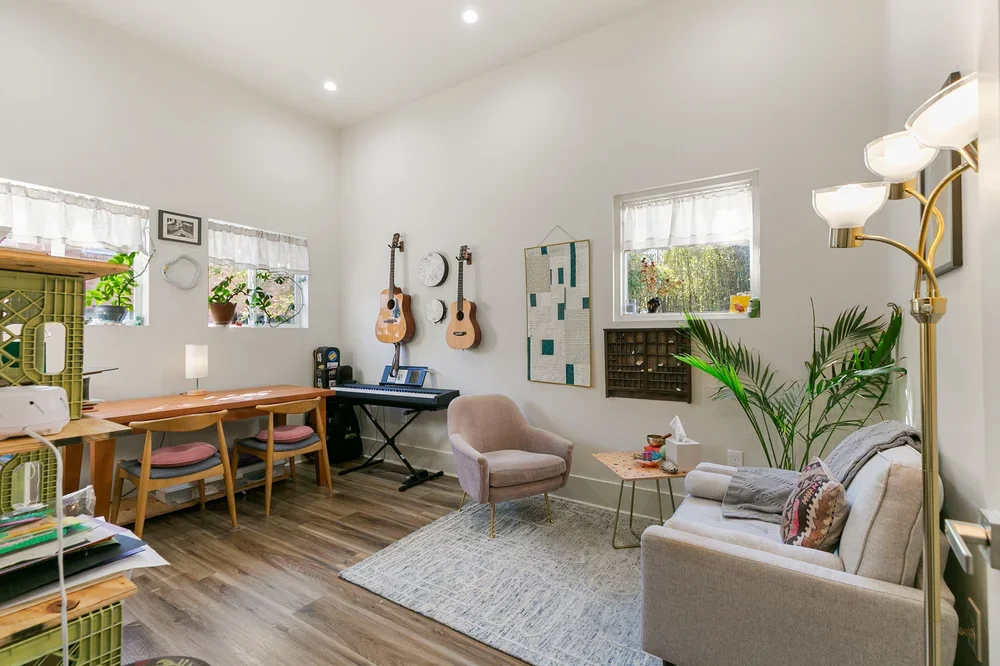 private boutique office rental new orleans Louisiana wooden desk with chairs, pink armchair, gray rug, gray sofa, plants guitars, natural light shelves, coffee tables, piano, music studio, music lesson new orleans