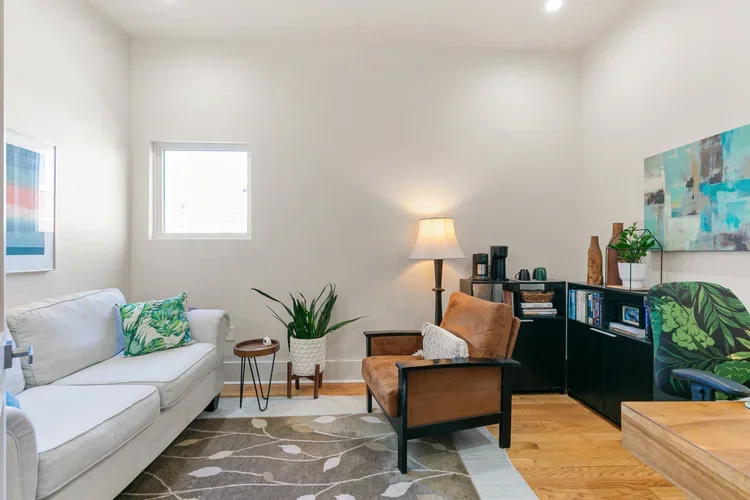 private commercial boutique office rental new orleans brown leather chair gray rug with leaf pattern white couch with accent pillows brown wood side table snake plant lamp framed art bookshelf office space