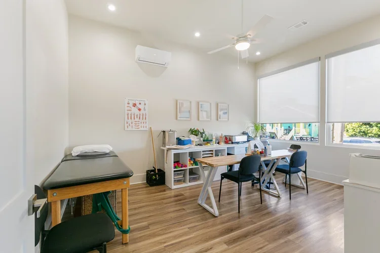 physical therapist private office space rental commercial boutique new orleans physical therapist office rental desk with chairs and white bookshelf white walls with framed art and pt bed for physical therapy in new orleans