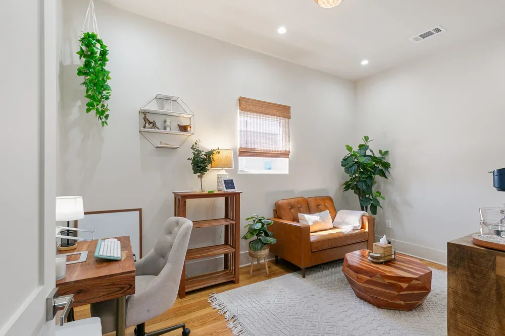 private commercial boutique office rental new orleans brown leather couch wooden coffee table wooden desk natural light windows bookshelf tall plant hanging plant white jute rug
