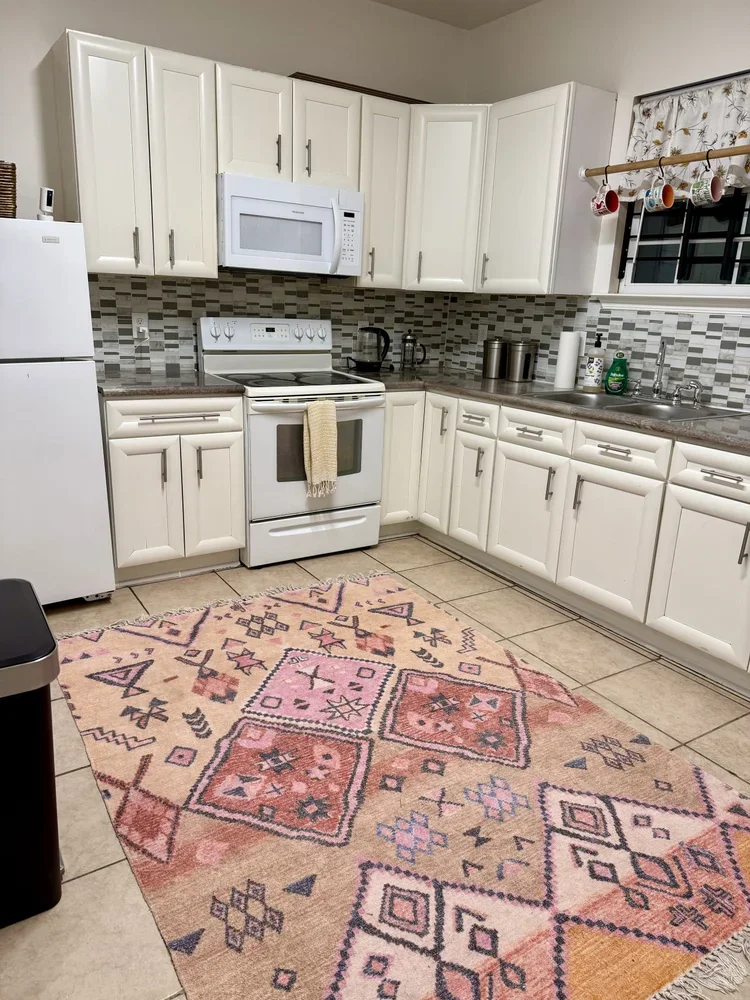 kitchen in private office rental suite commercial office rentals in new orleans white trim kitchen with granite countertops, microwave, oven, stove, fridge woven pink and tan moroccan style rug with mugs and curated space