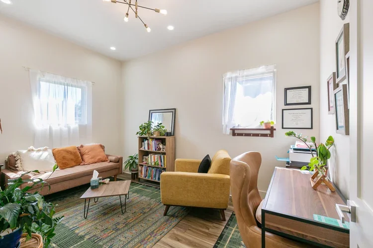 private commercial office rental new orleans wooden desk leather desk chair windows natural light leather sofa couch wooden coffee table white walls light fixture wooden bookshelf framed art mustard yellow armchair green moroccan rug
