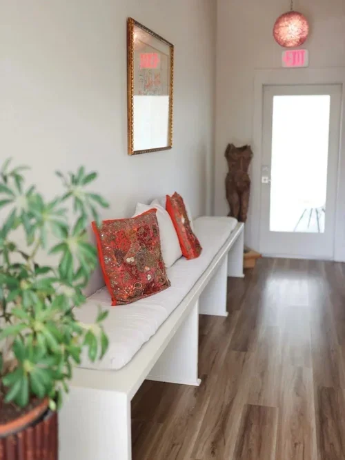 New orleans private boutique commercial office space for rent waiting room lobby white bench white cushions red pillows nude statue framed artwork natural light glass door wooden floors white walls plants