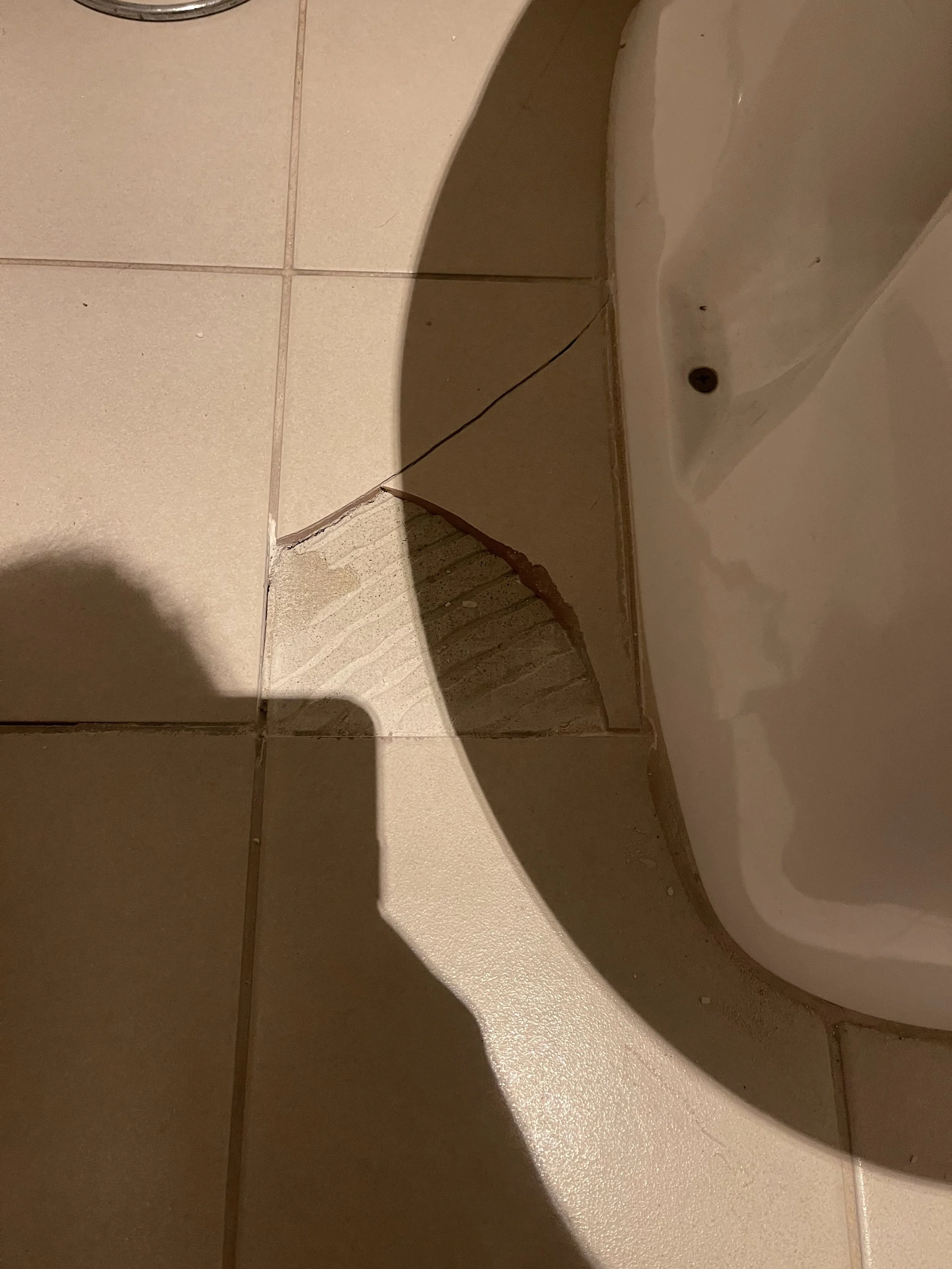 Broken or damaged bathroom floor tiles and baseboard near a toilet.