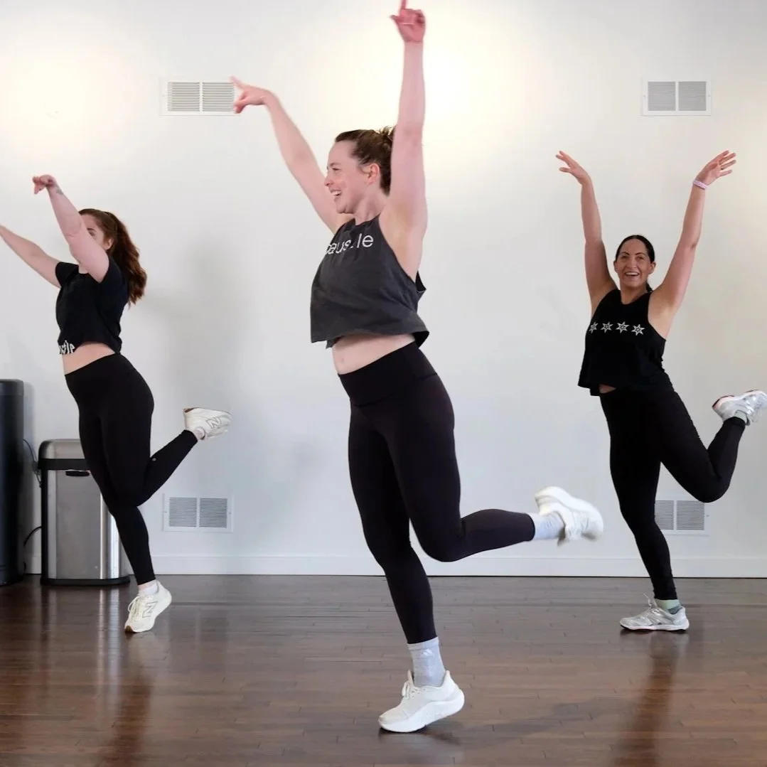 Three women dancing with their hands in the air and feet kicked up.