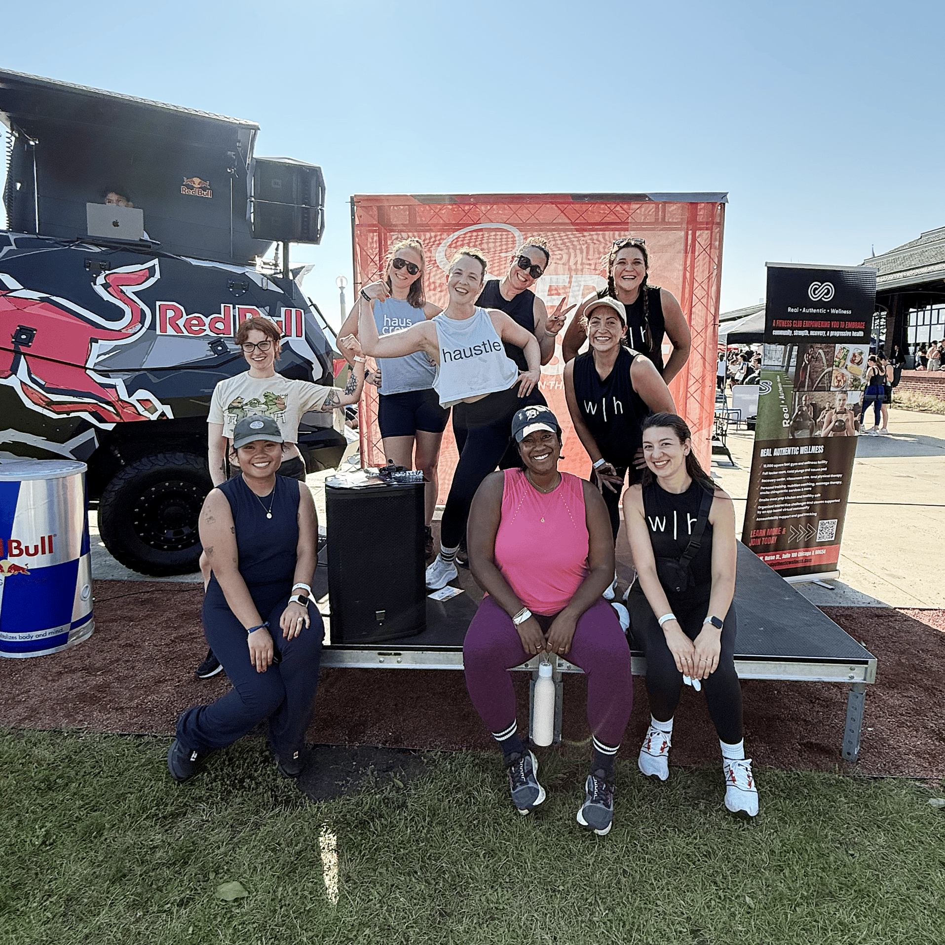 A group of women smiling and posing on stage at an outdoor fitness event.