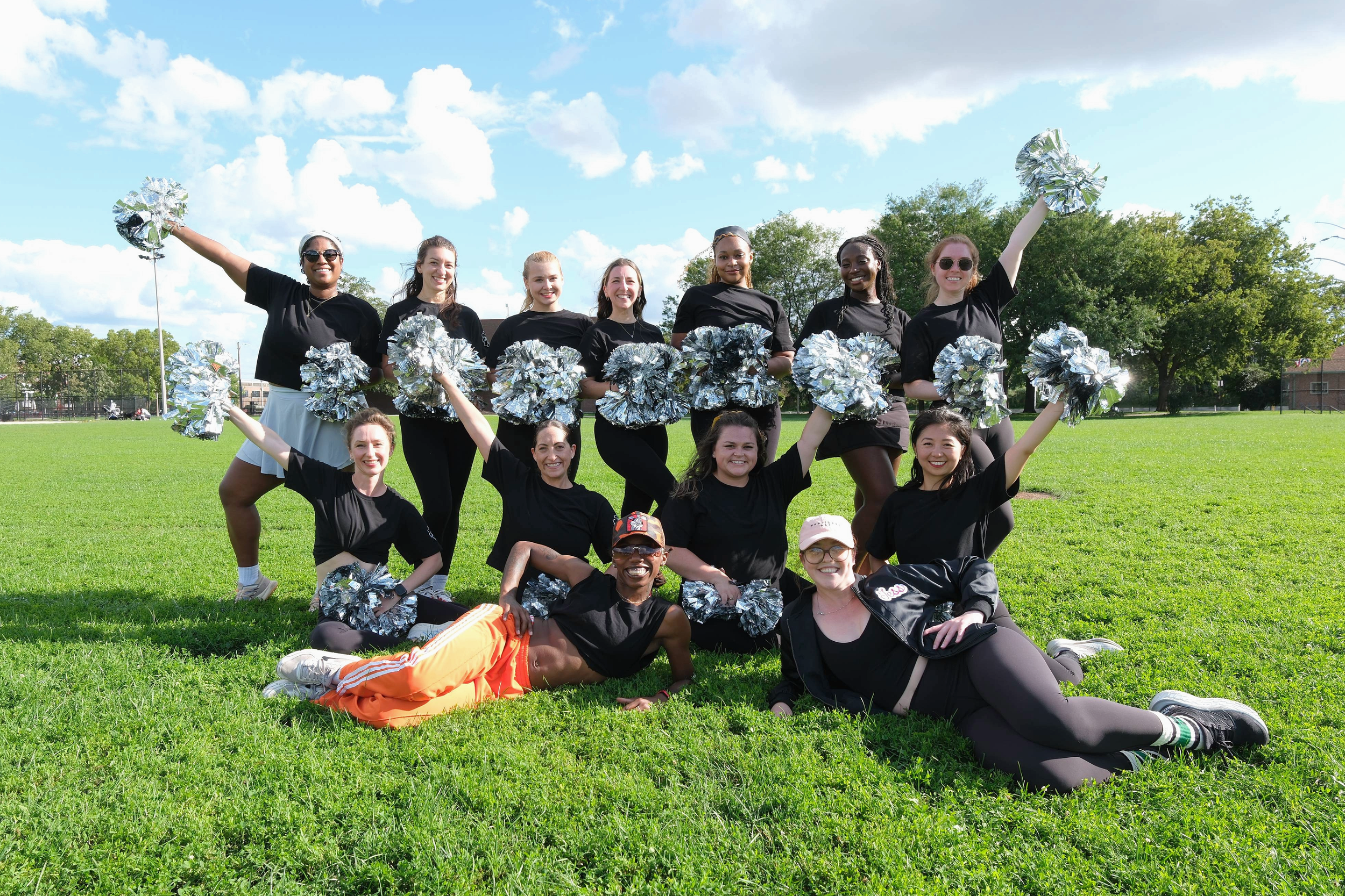 A group of women pose on a field with matching uniforms and pom poms.