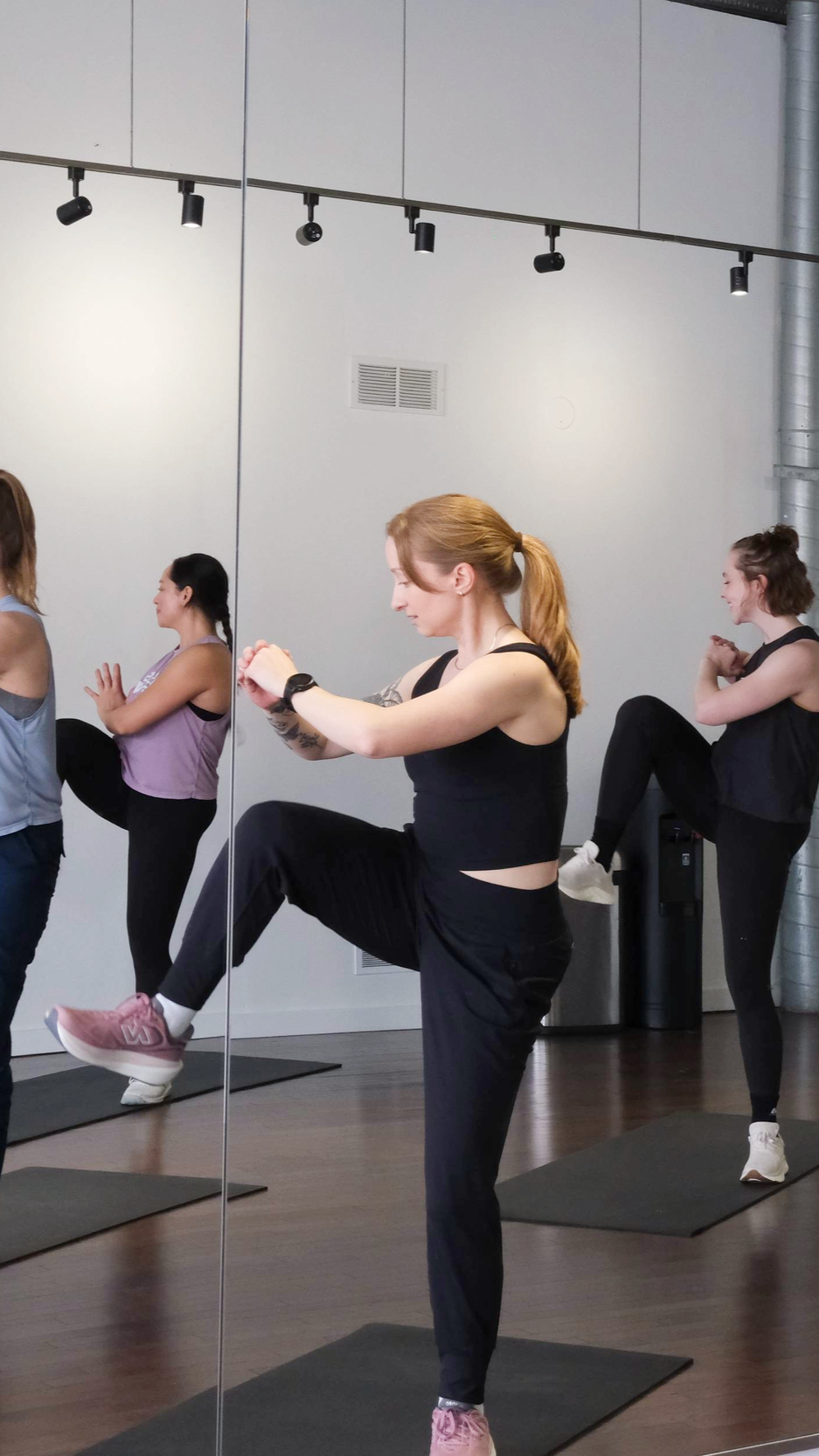Women on fitness mats doing intense standing core exercises.
