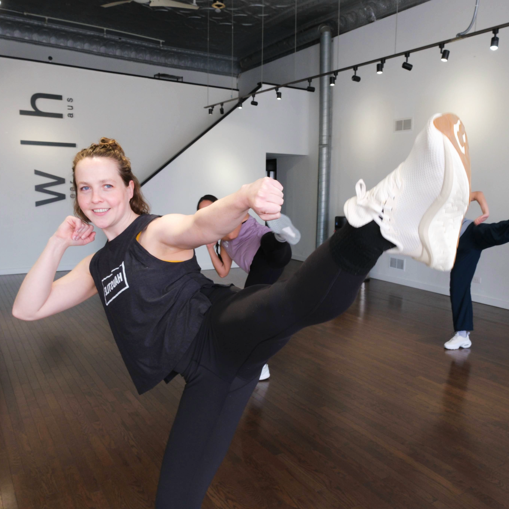 Woman teaching a kickboxing class, kicking her foot in the air while punching.