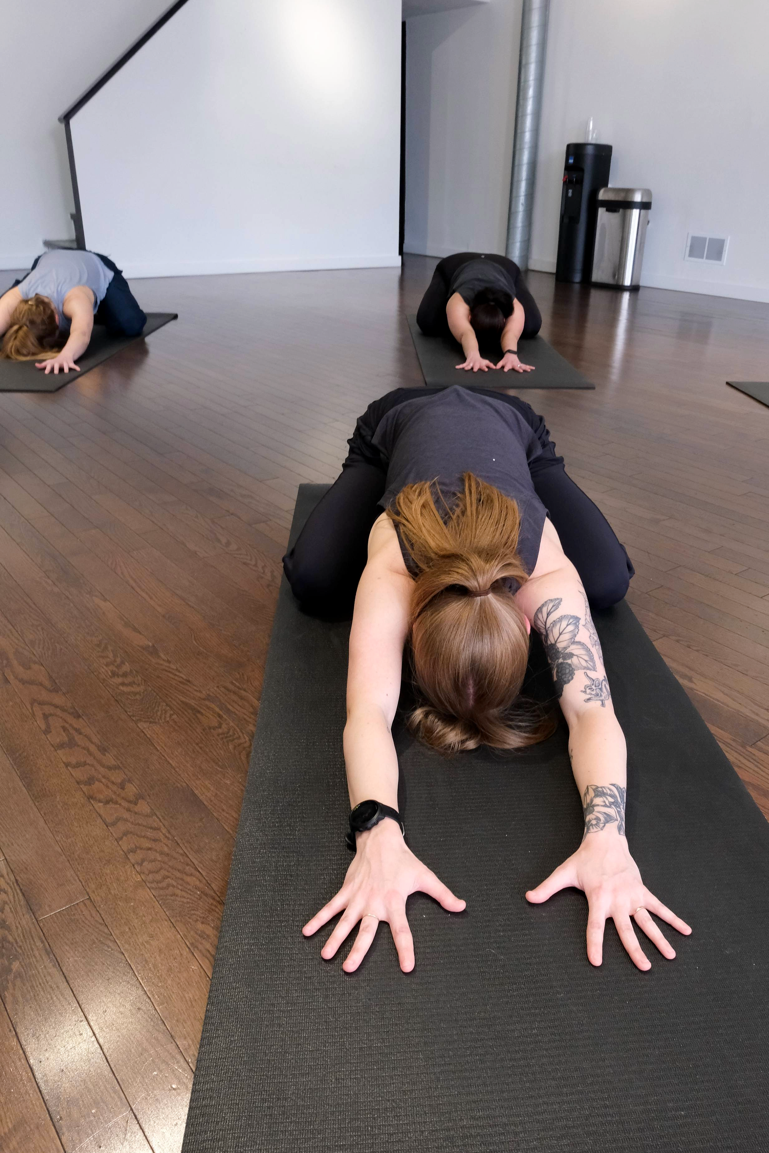 Woman with a ponytail leads a relaxing yoga stretch on a mat.